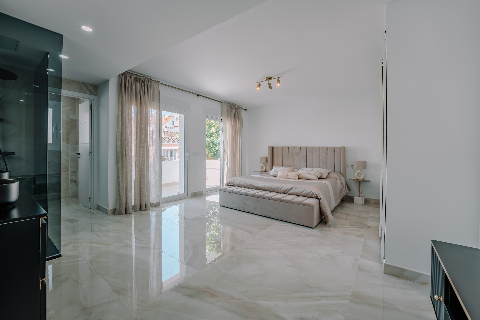 Bedroom with a large bed, marble-patterned floor, and glass patio doors. A modern shower enclosure is on the left.