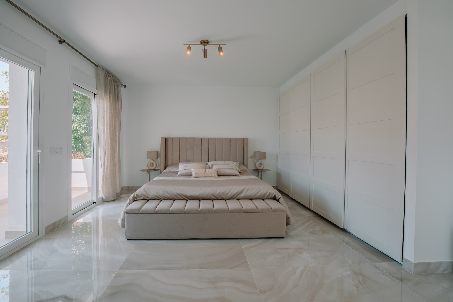Centrally aligned view of a primary bedroom with a large bed, built-in wardrobes, and glass doors to a terrace.