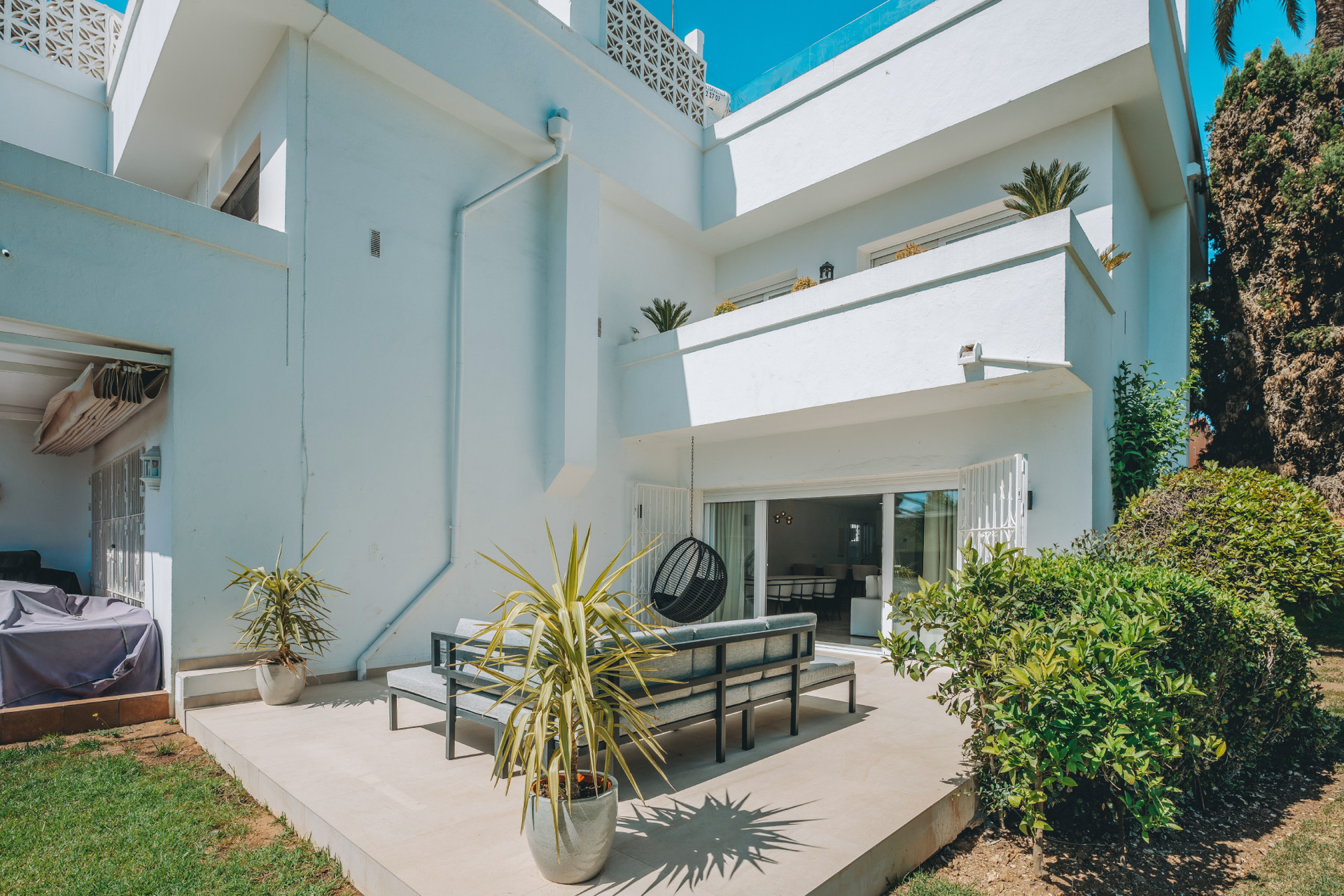 White modern townhouse exterior with a ground-floor patio featuring outdoor seating and lush greenery.