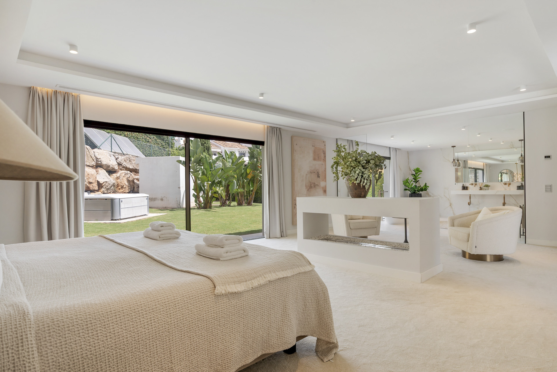Master bedroom view showcasing large windows, plush bedding, and a serene garden outlook with greenery.