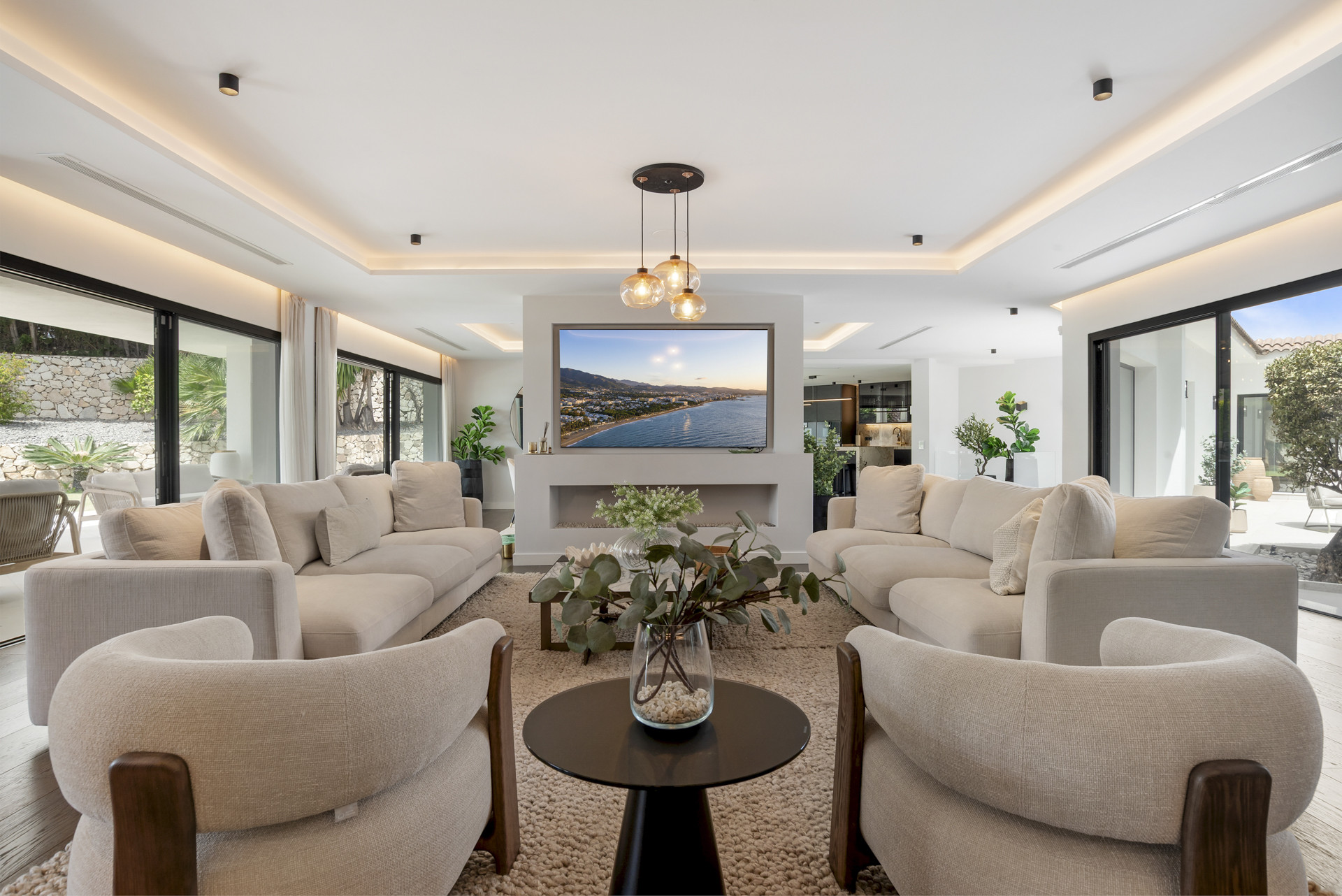 Spacious living room with large windows, soft beige sofas, and a wall-mounted TV.