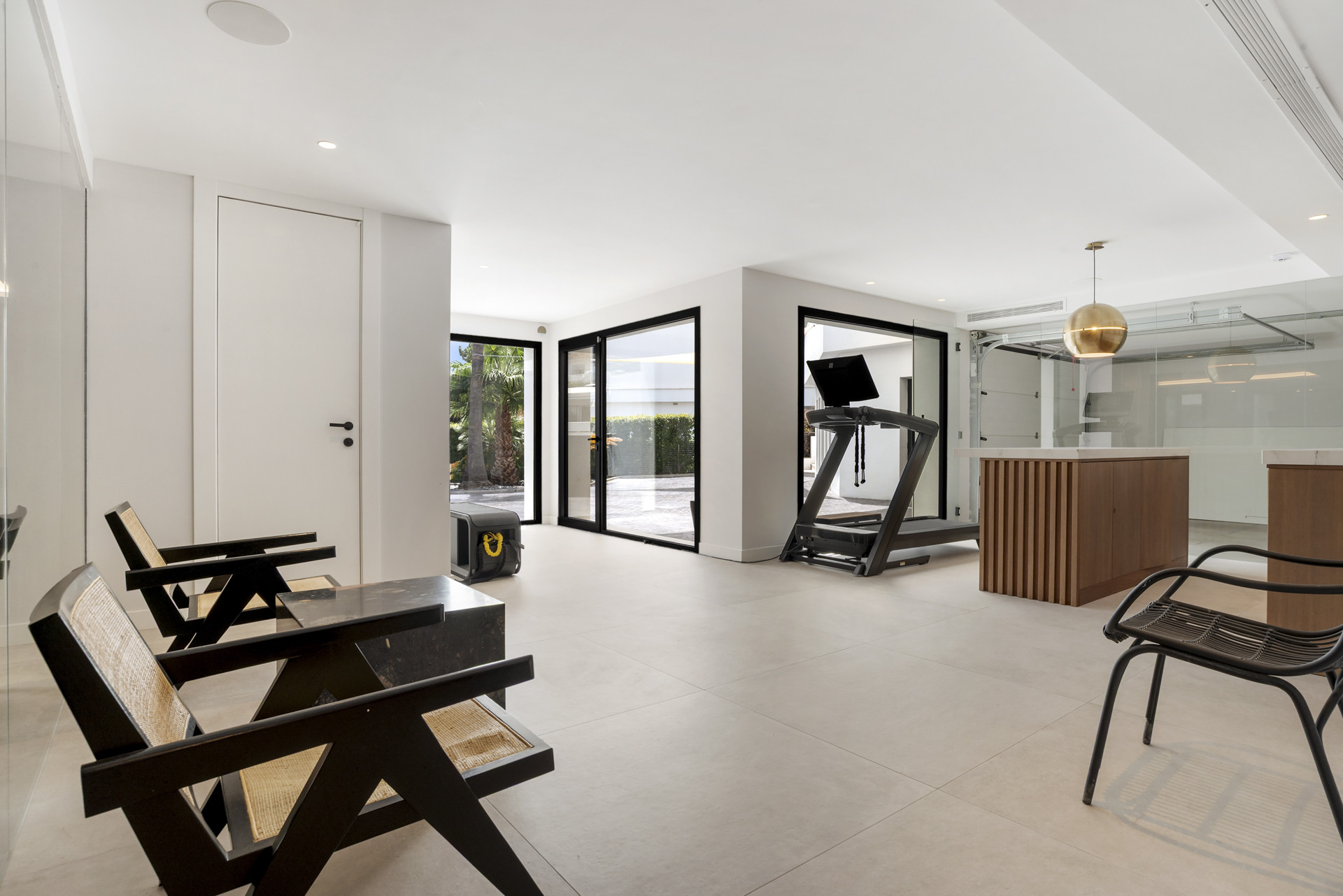Modern fitness area with treadmill and cabinetry, large glass doors leading outdoors.