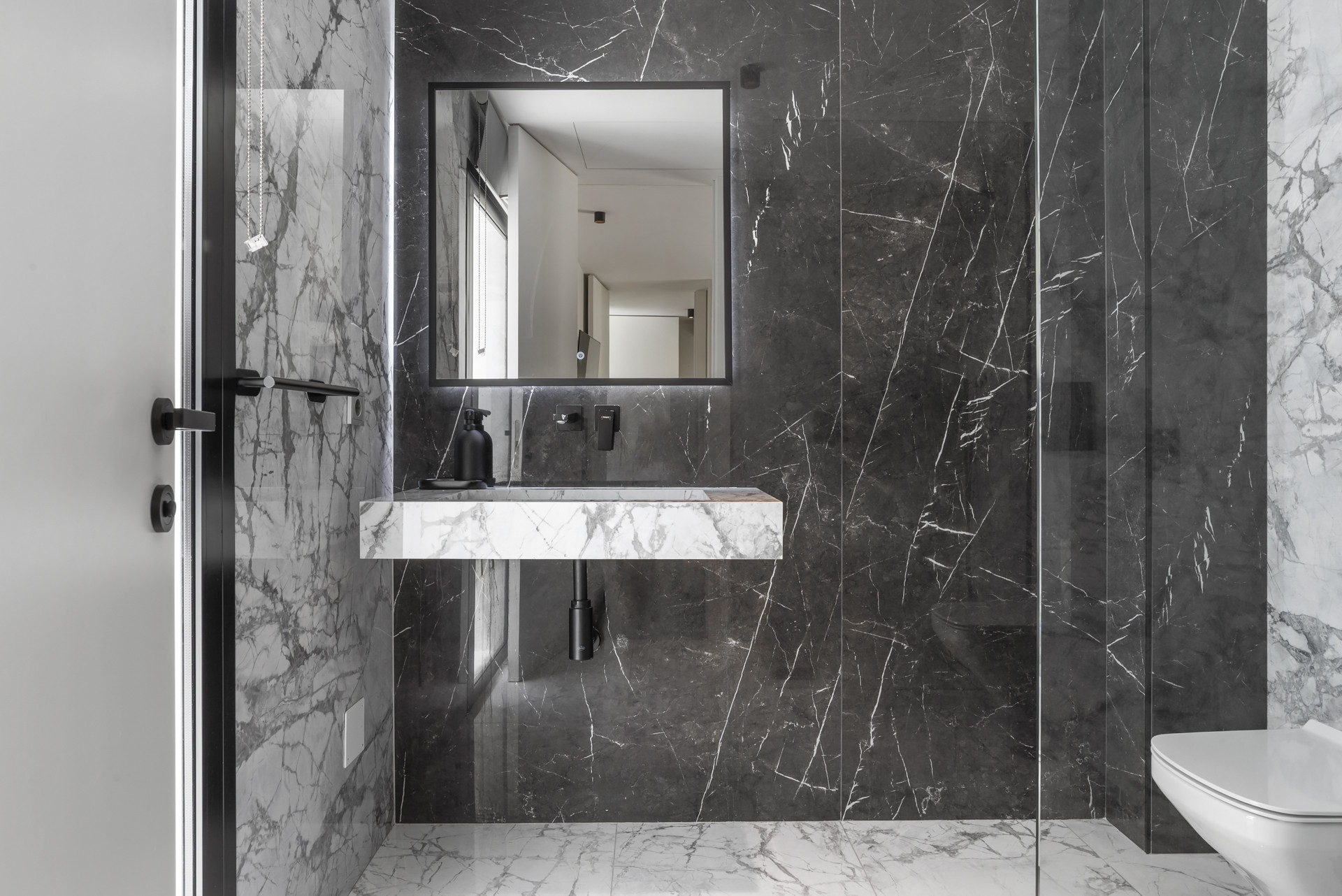 Stylish bathroom with dark marble walls and an integrated sink area next to a glass shower.