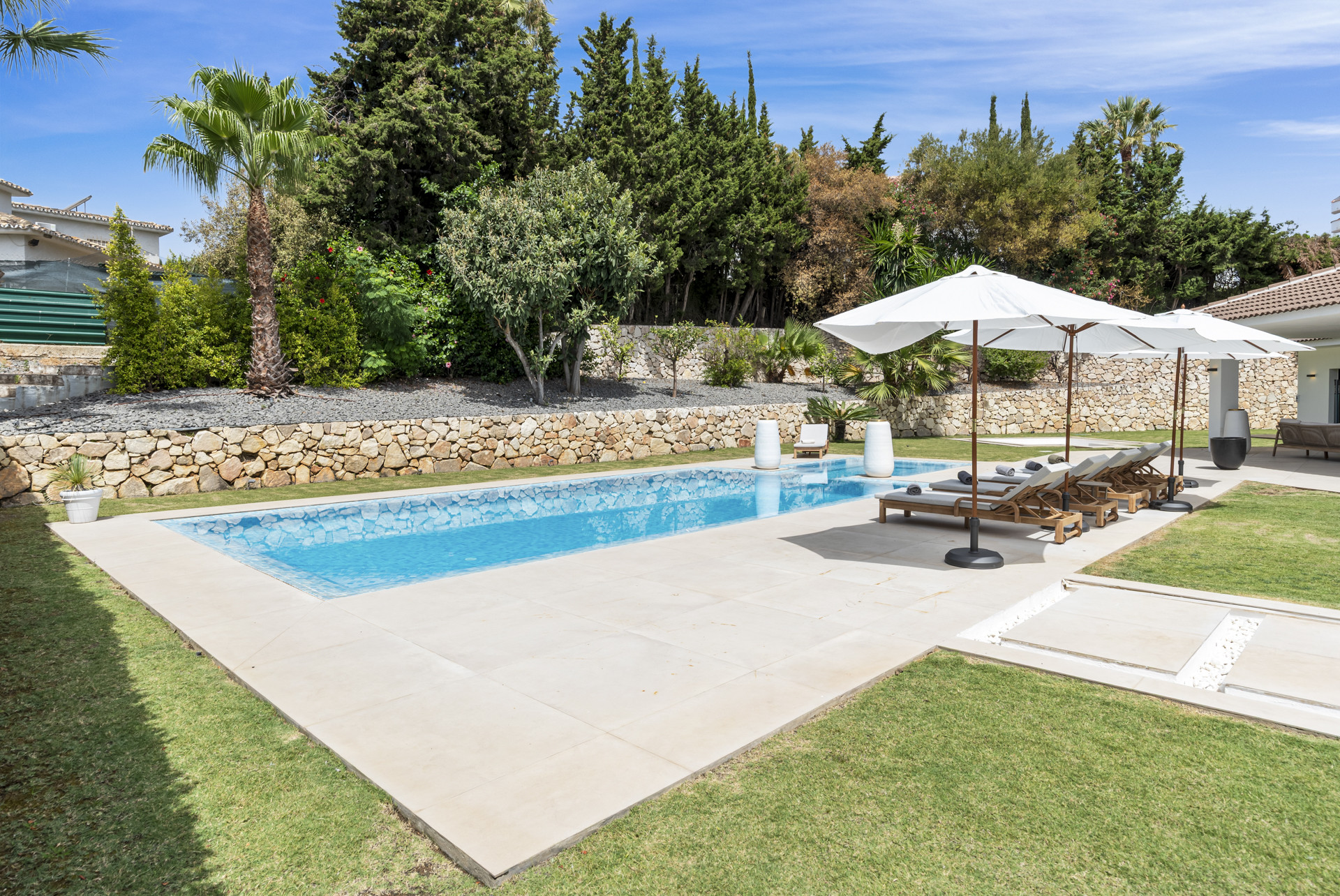 View of the pool area with loungers and umbrellas surrounded by landscaping.