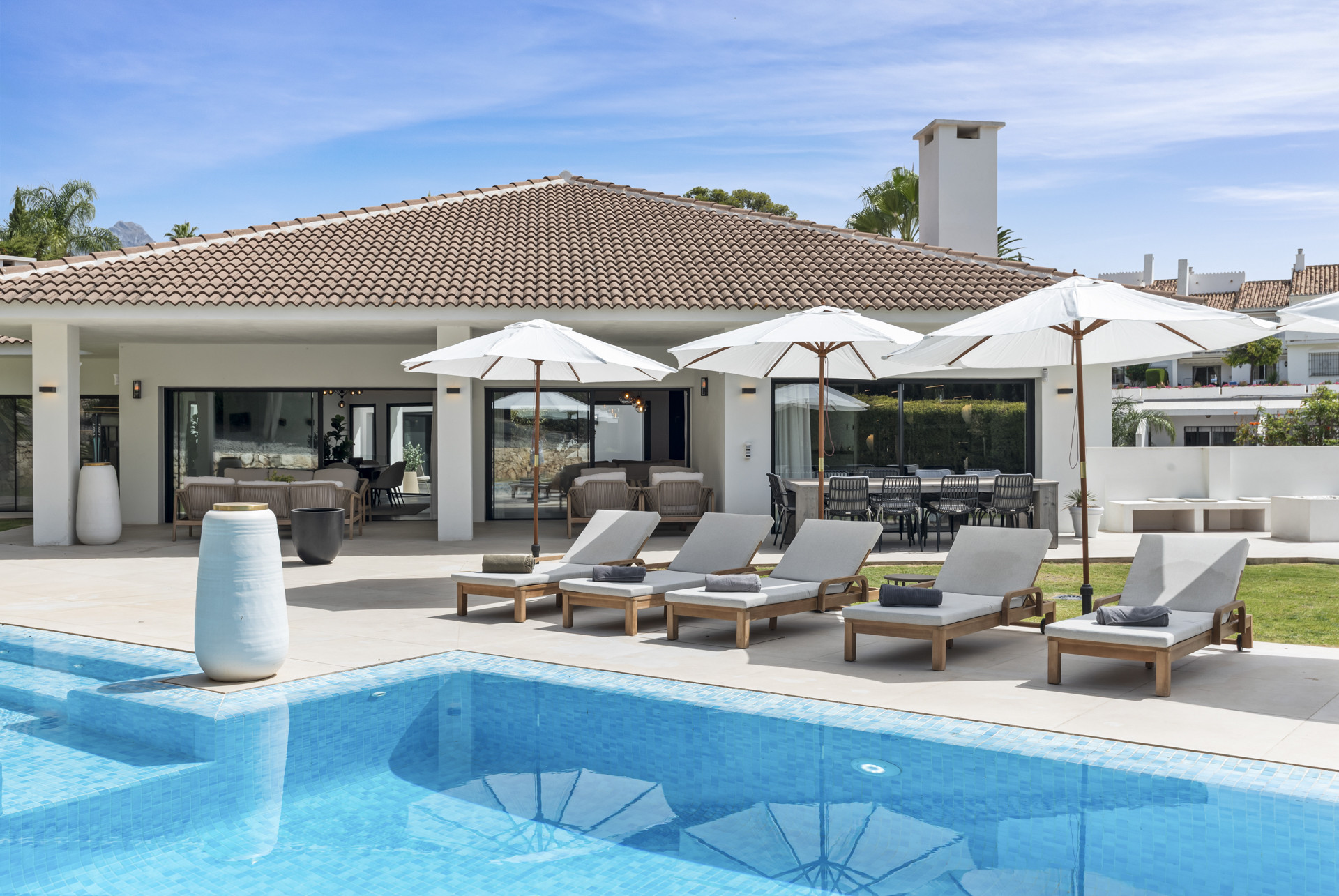Outdoor area with sun loungers, umbrellas, and a pool adjacent to the house.