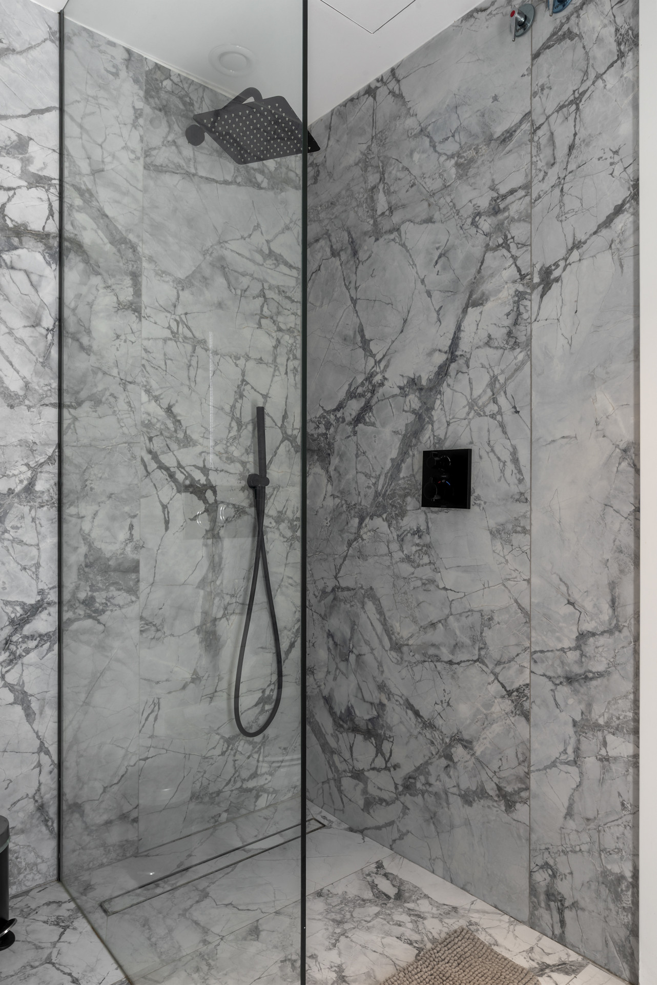 Elegant marble shower space with a glass enclosure and rainforest showerhead.