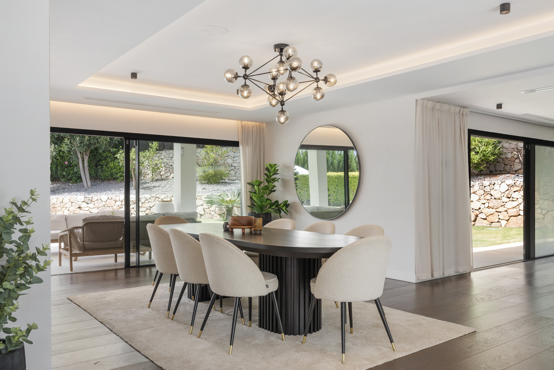 Dining area with large table, circular mirror, modern chandelier, and access to outside.