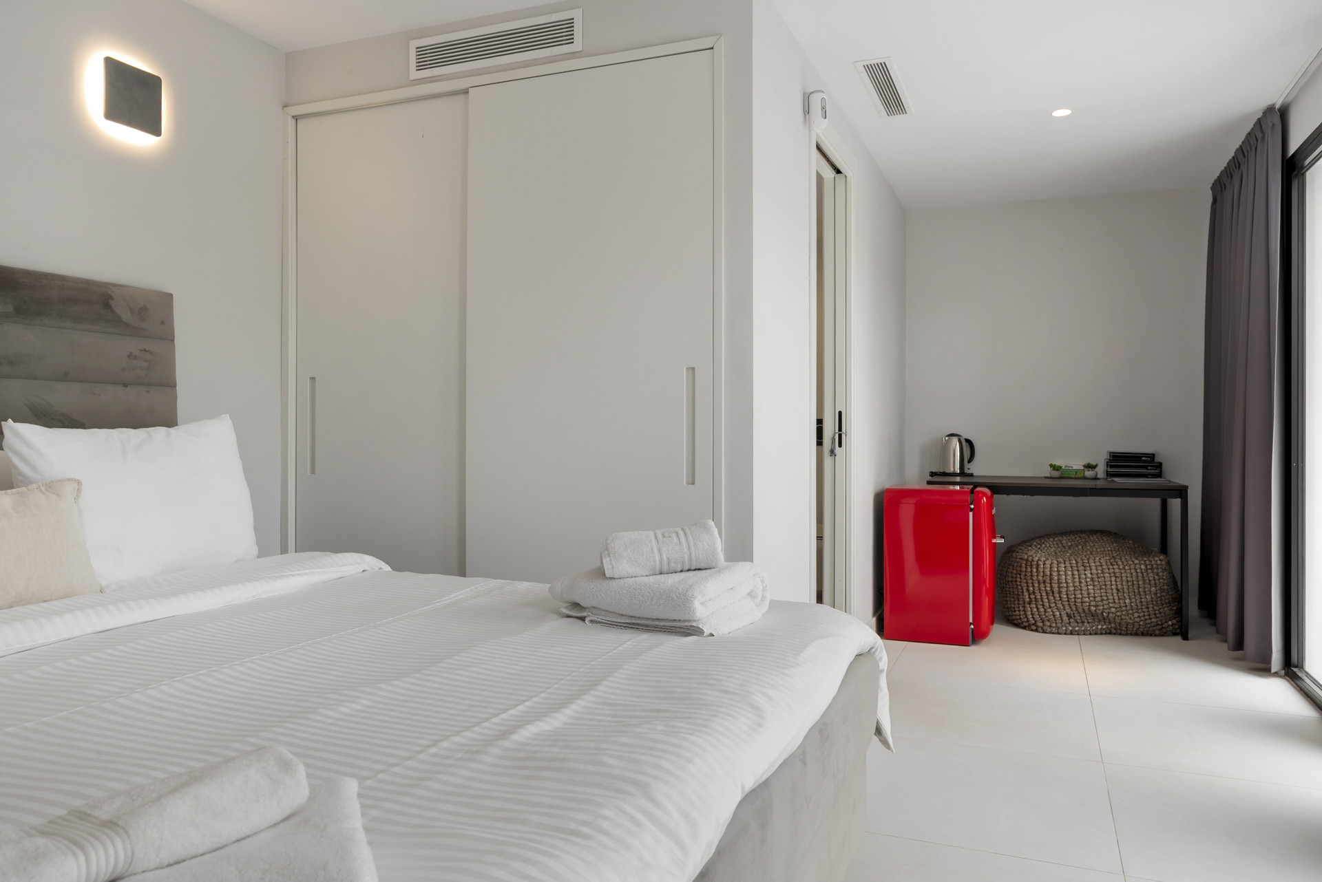 Guest bedroom with built-in closet, red mini fridge, and workspace.