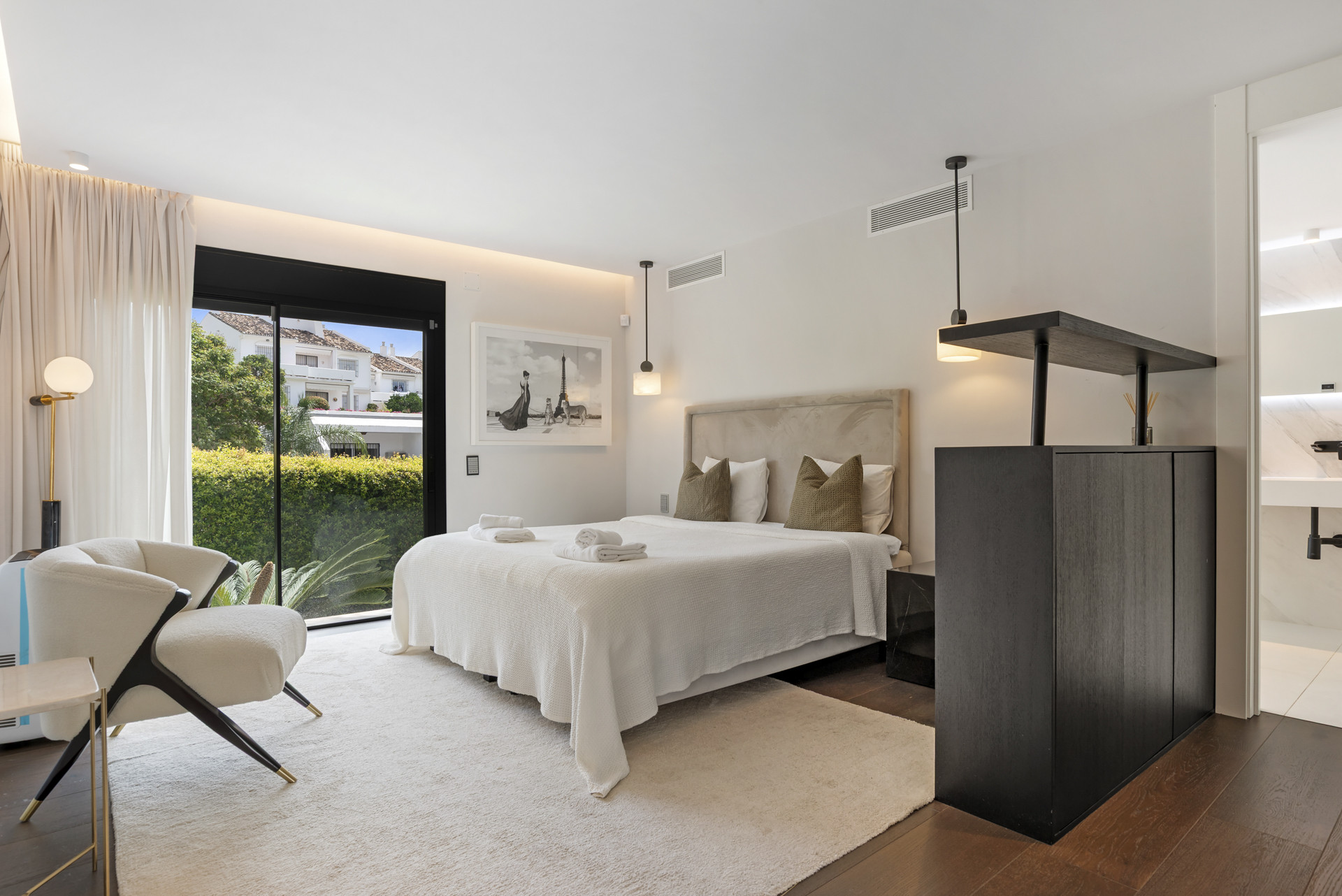 Elegant bedroom featuring a king bed, armchair, and glass door to outdoor view.