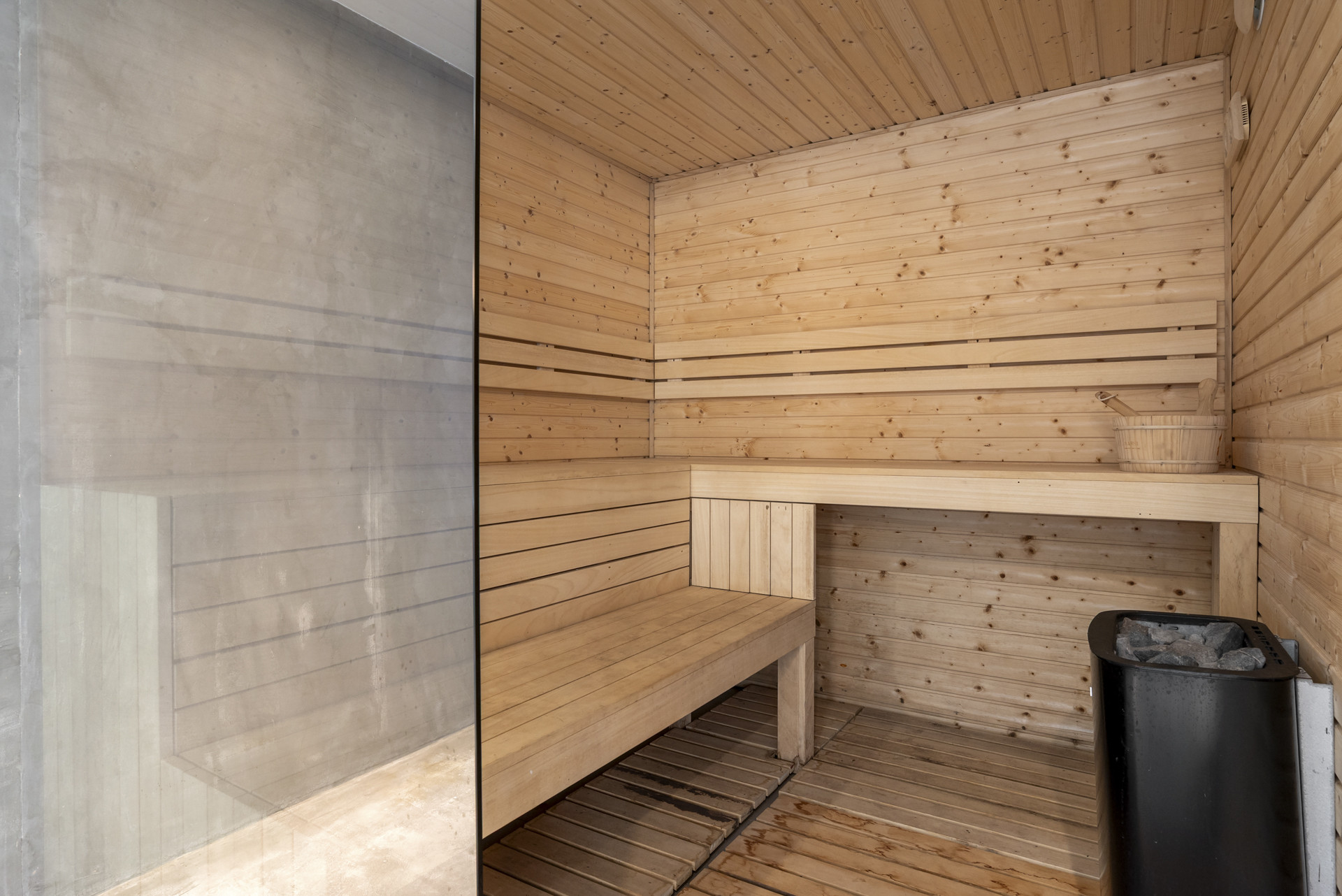 Wooden sauna with bench seating, natural wood paneling, and a small bucket for water.