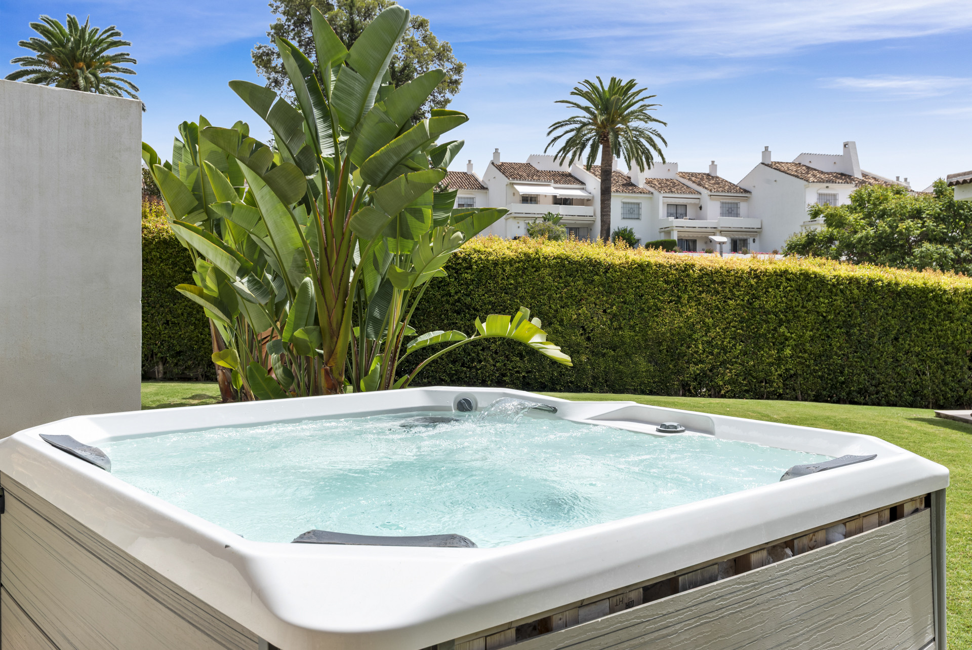 Hot tub surrounded by greenery with palm trees in the background.
