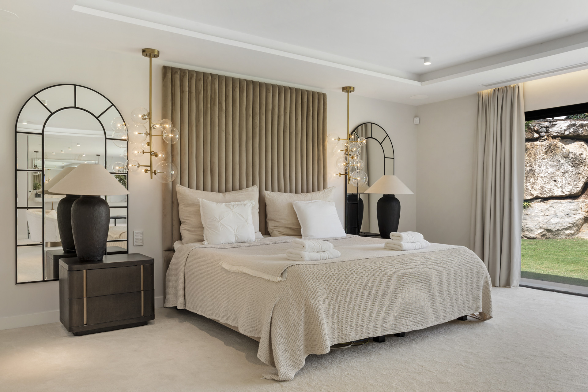 Luxurious bedroom with a plush headboard, decorative lighting, and garden access.