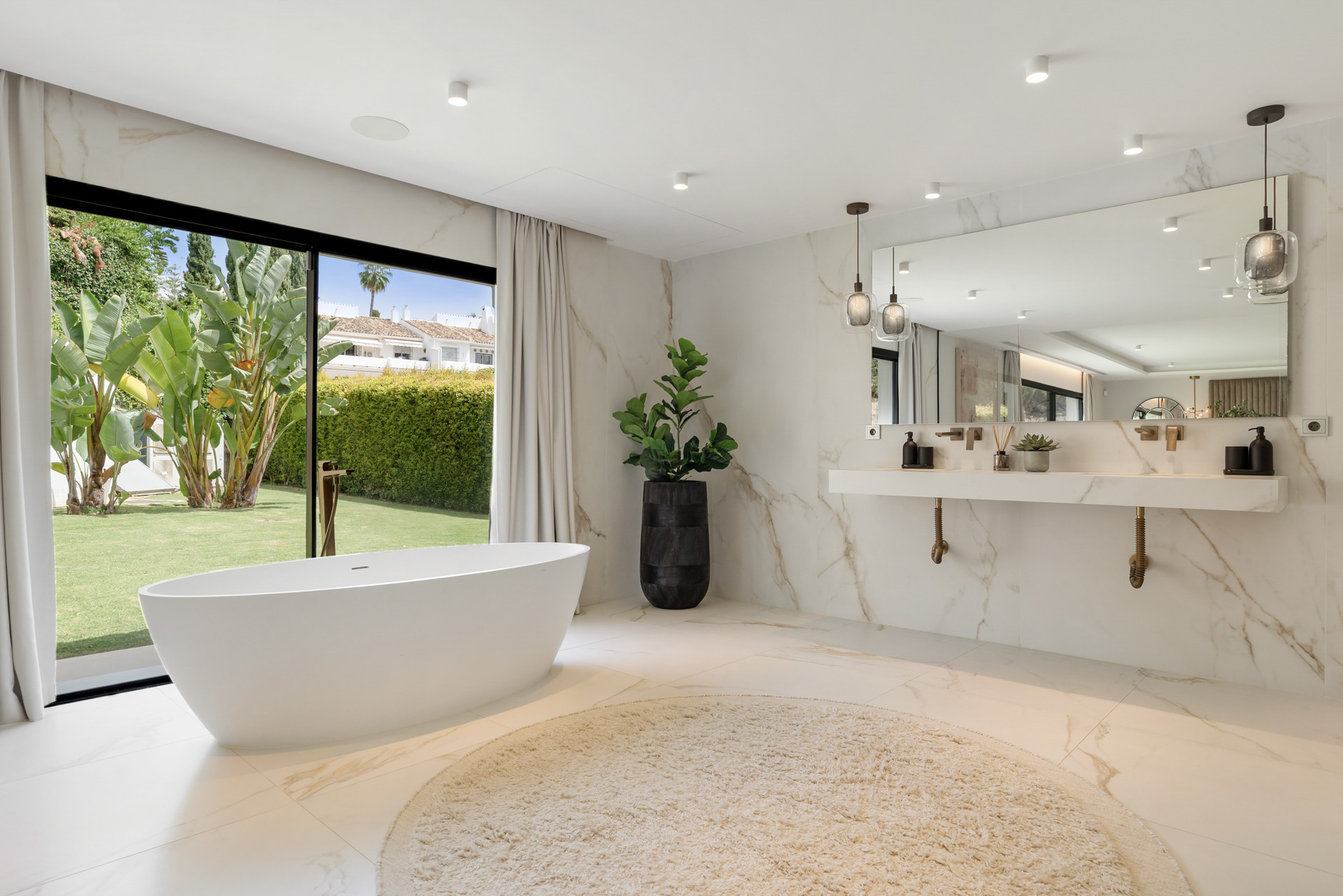 Bathroom features a freestanding tub, elegant marble details, and an outdoor view of landscaped greenery.