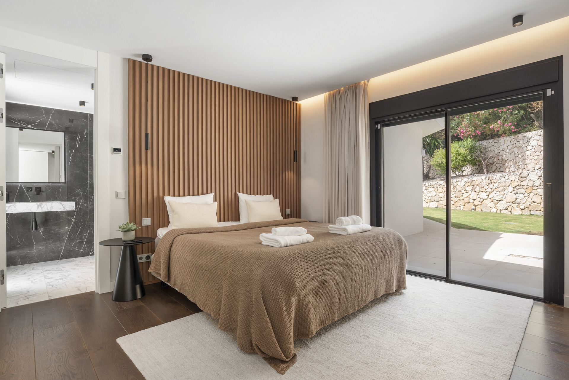 Spacious bedroom with wood accent wall, large sliding doors, and two made beds with towels.