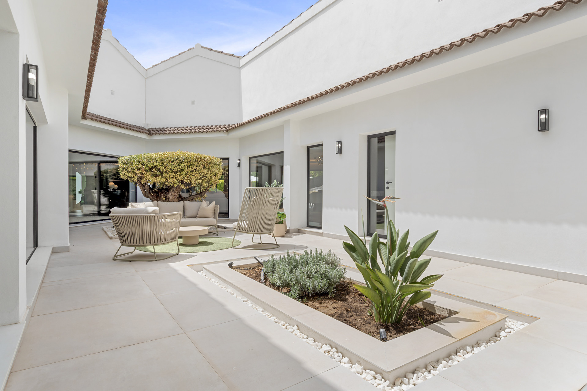 Outdoor courtyard with seating area, potted plants, and a central planter surrounded by light walls.