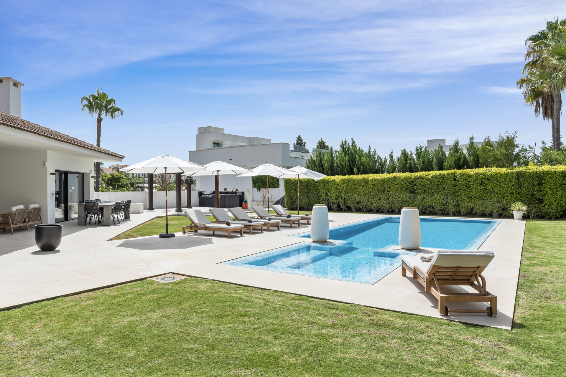 Outdoor area showcasing swimming pool, sun loungers, and umbrellas surrounded by lush greenery.