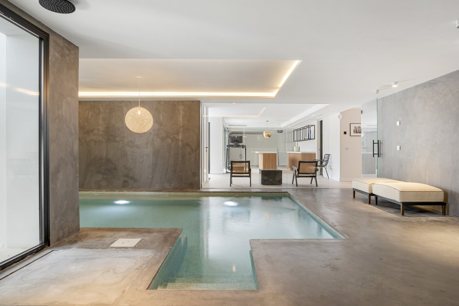 Perspective of pool area with furniture, looking towards fitness space through glass wall.
