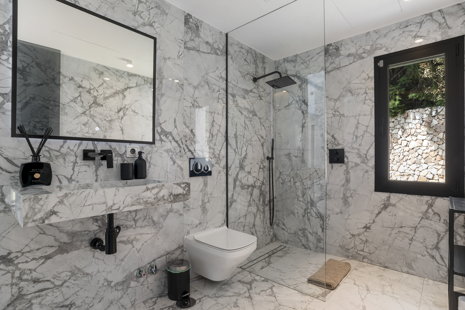 Modern bathroom featuring marble walls and a glass shower enclosure with rainfall showerhead.