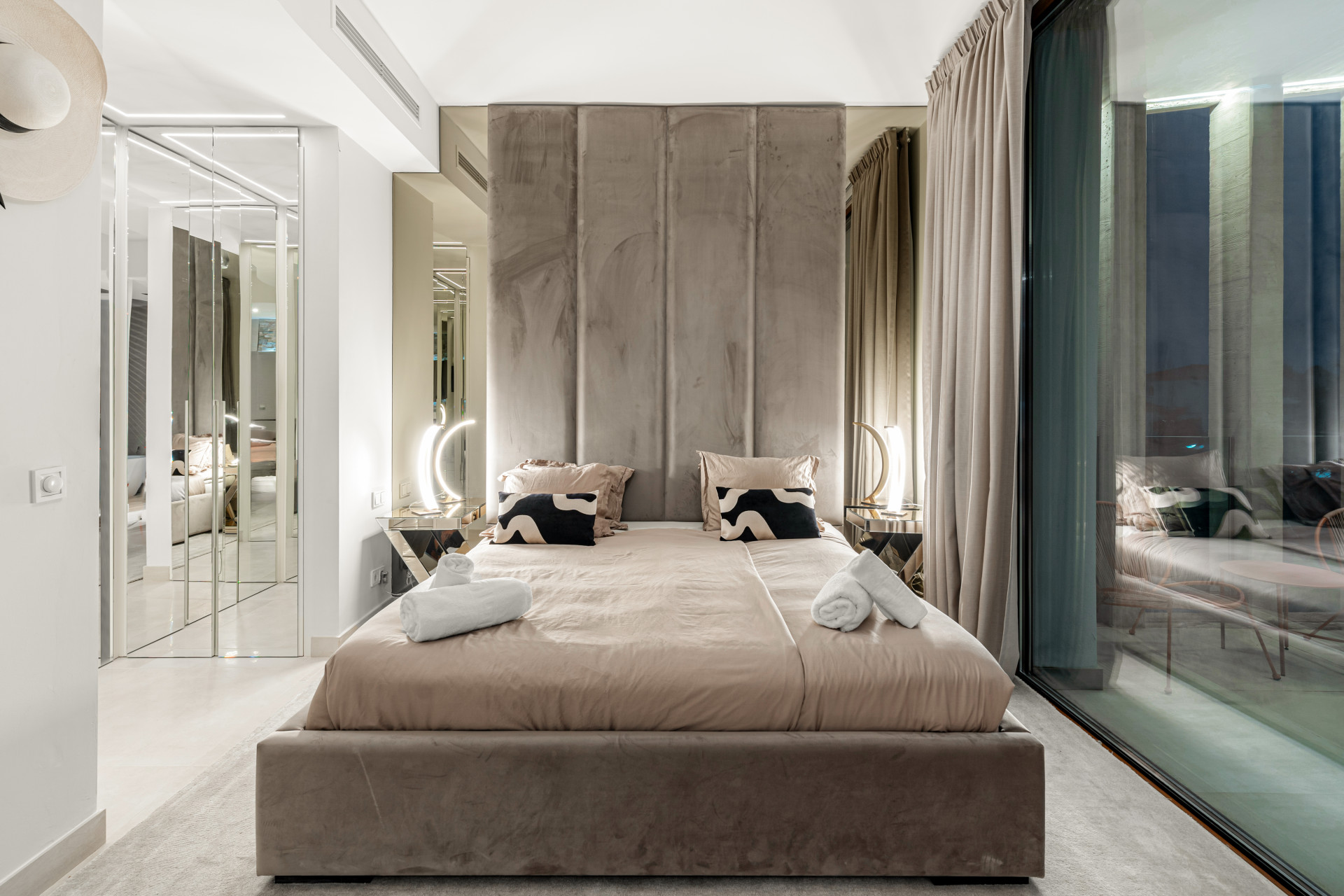 Stylish bedroom with mirrored wall, contemporary lamps, and large window.