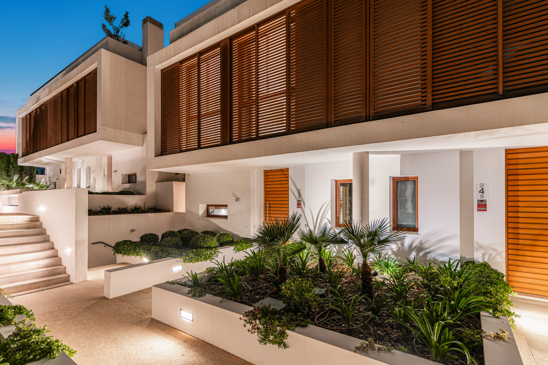 Entry area with landscaped beds and wooden shutters on facade.