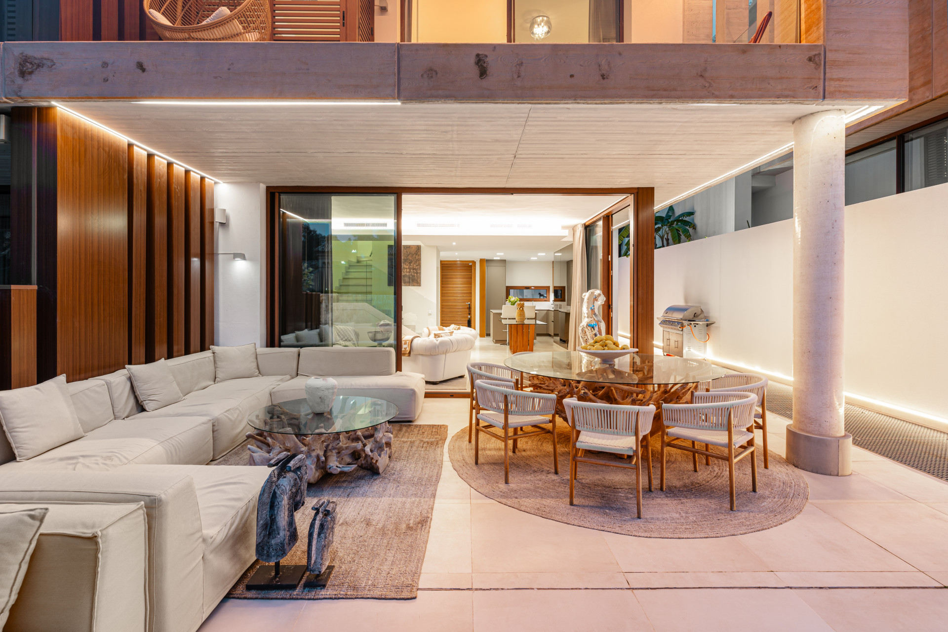 Outdoor dining area with a sectional sofa and a glass table with natural wood accents.