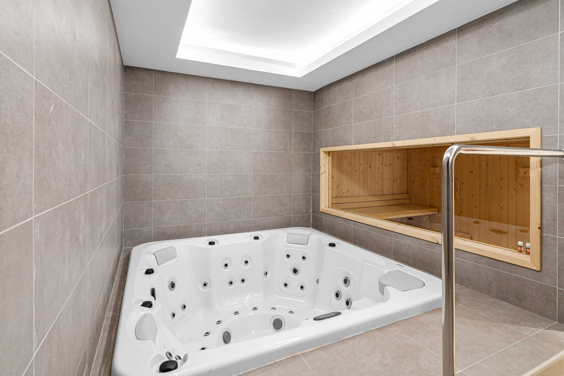 Interior view of a jacuzzi surrounded by tiled walls and a wooden sauna visible in the background.