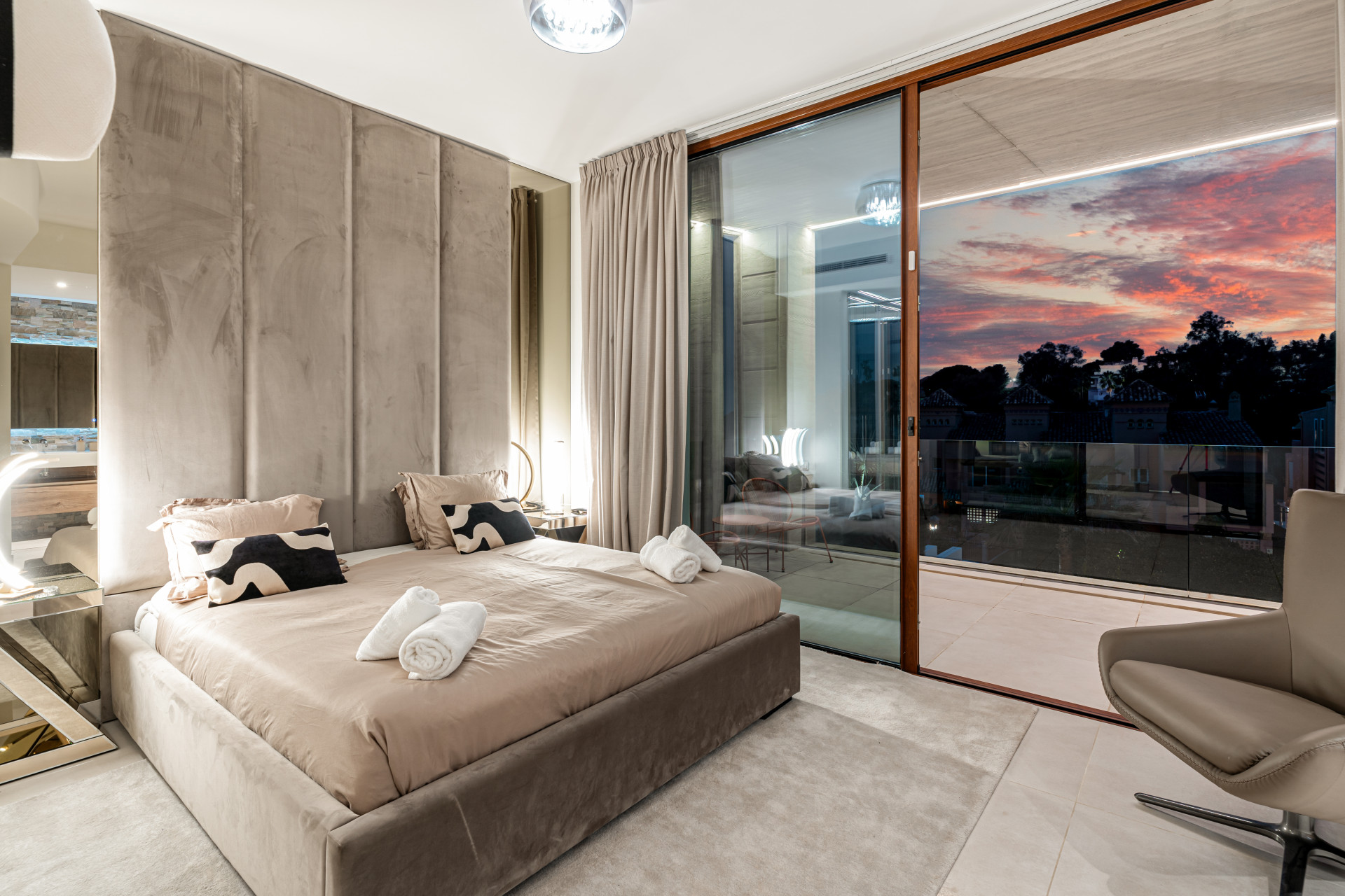 Cozy bedroom that showcases a sunset view through large glass doors, plush bedding and modern decor.