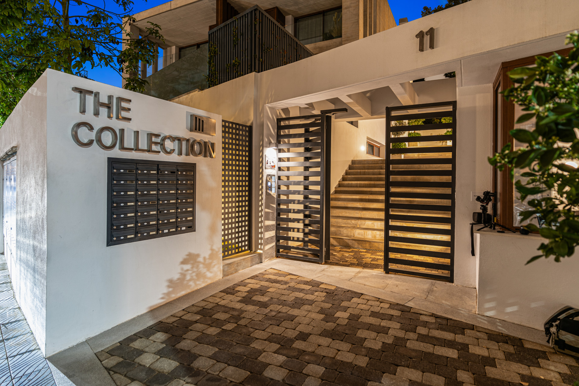 Entrance to a collection of residences with mailboxes and a staircase visible behind modern gates.