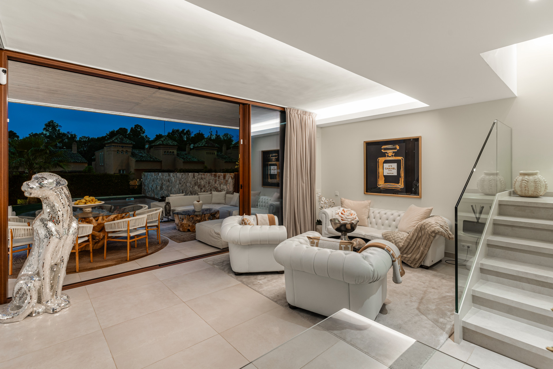 Living room with white sofas and a decorative glass figure by the stairs.