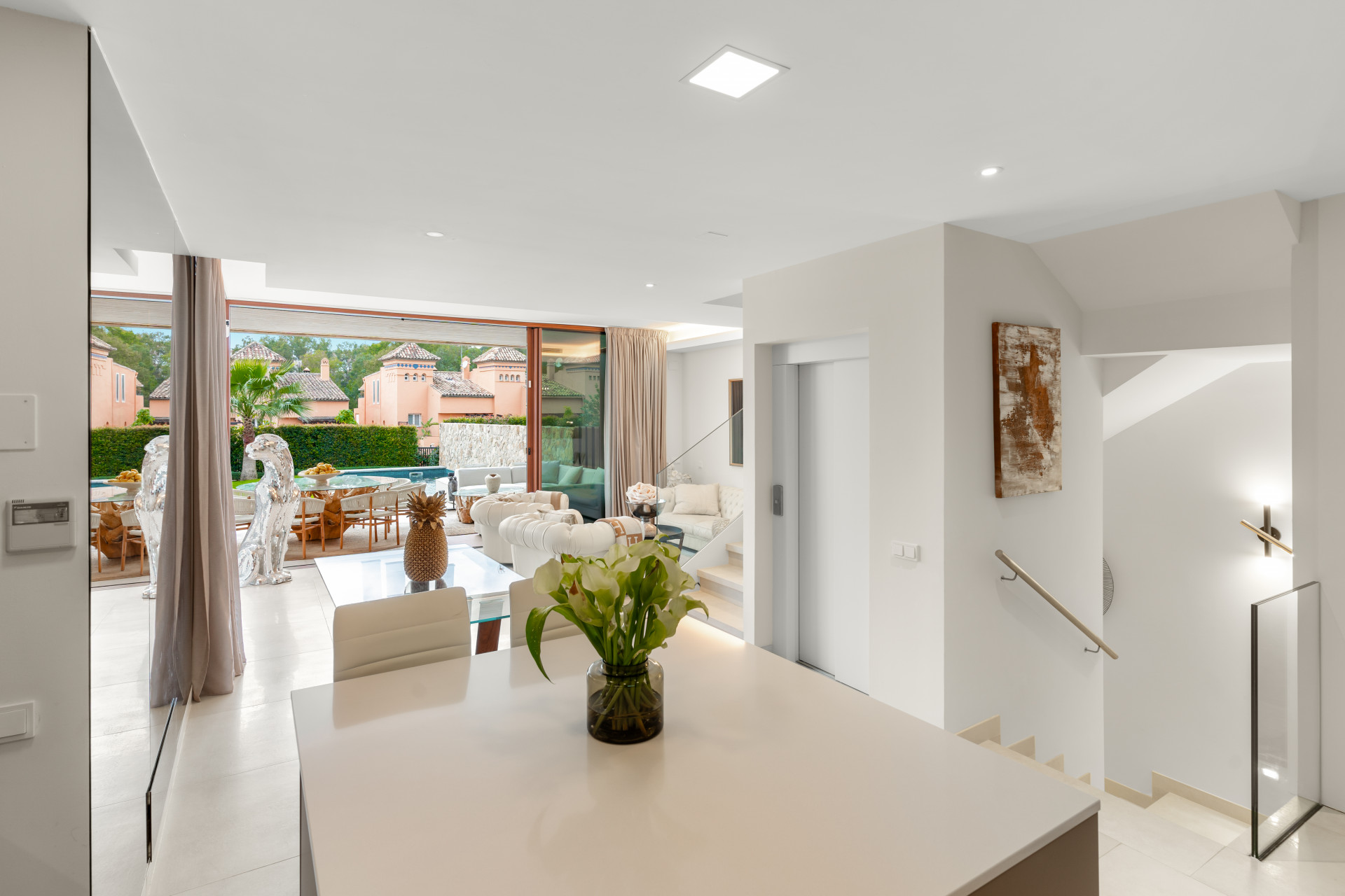 Bright living area with large windows and sliding doors, leading to an outdoor dining space by the pool.