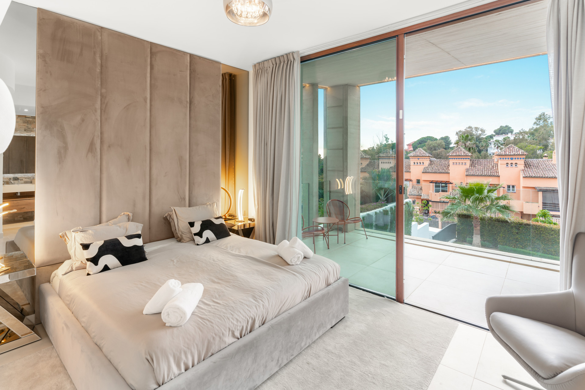 Elegant bedroom with twin beds, wall-mounted lighting, and direct access to a balcony overlooking greenery.