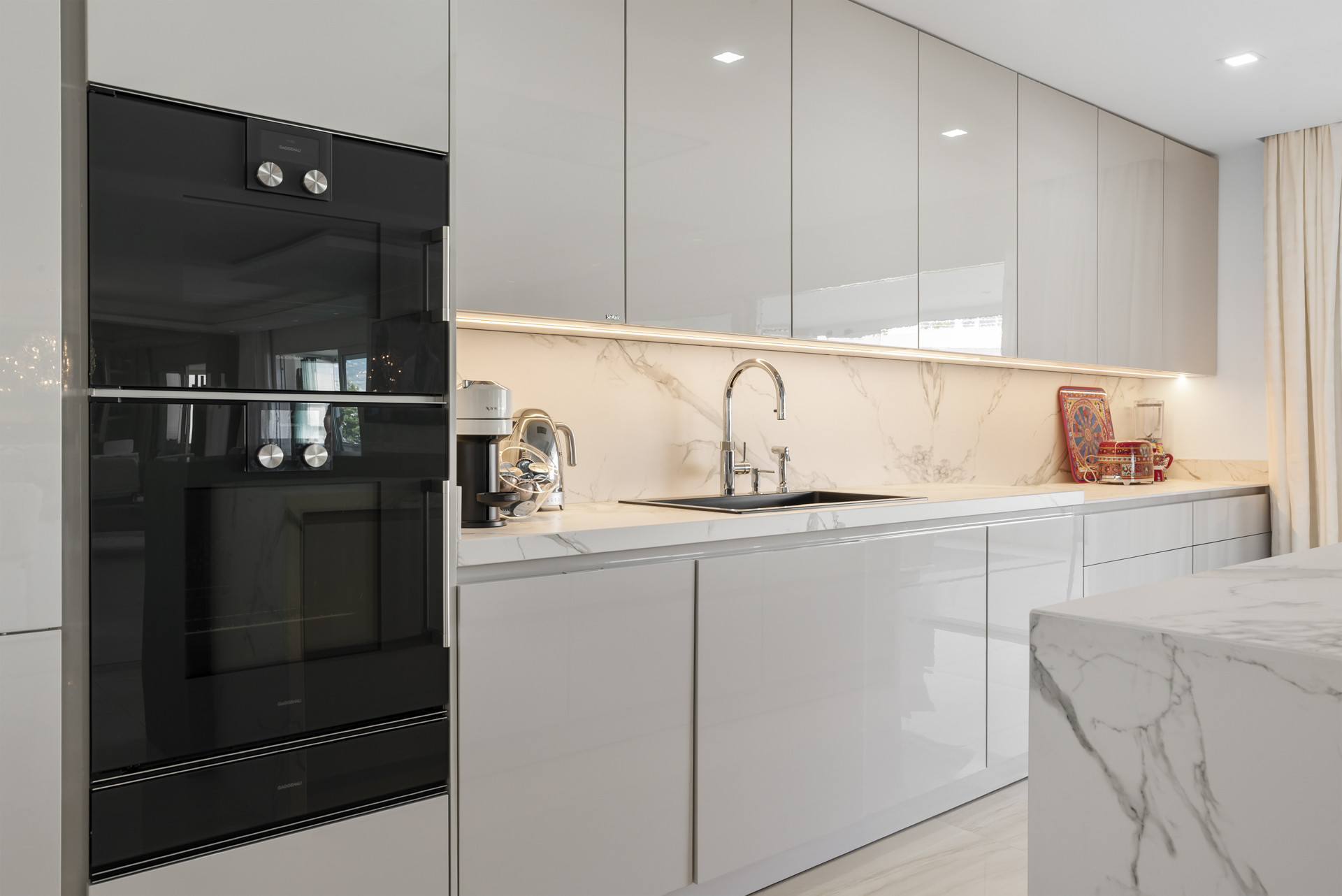 Modern kitchen with glossy cabinets and marble backsplash, featuring black appliances.