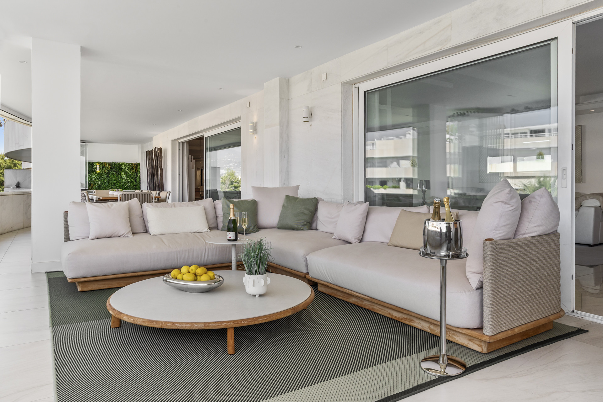 An open terrace with a large seating area, a low table, and a view towards an adjacent dining space.