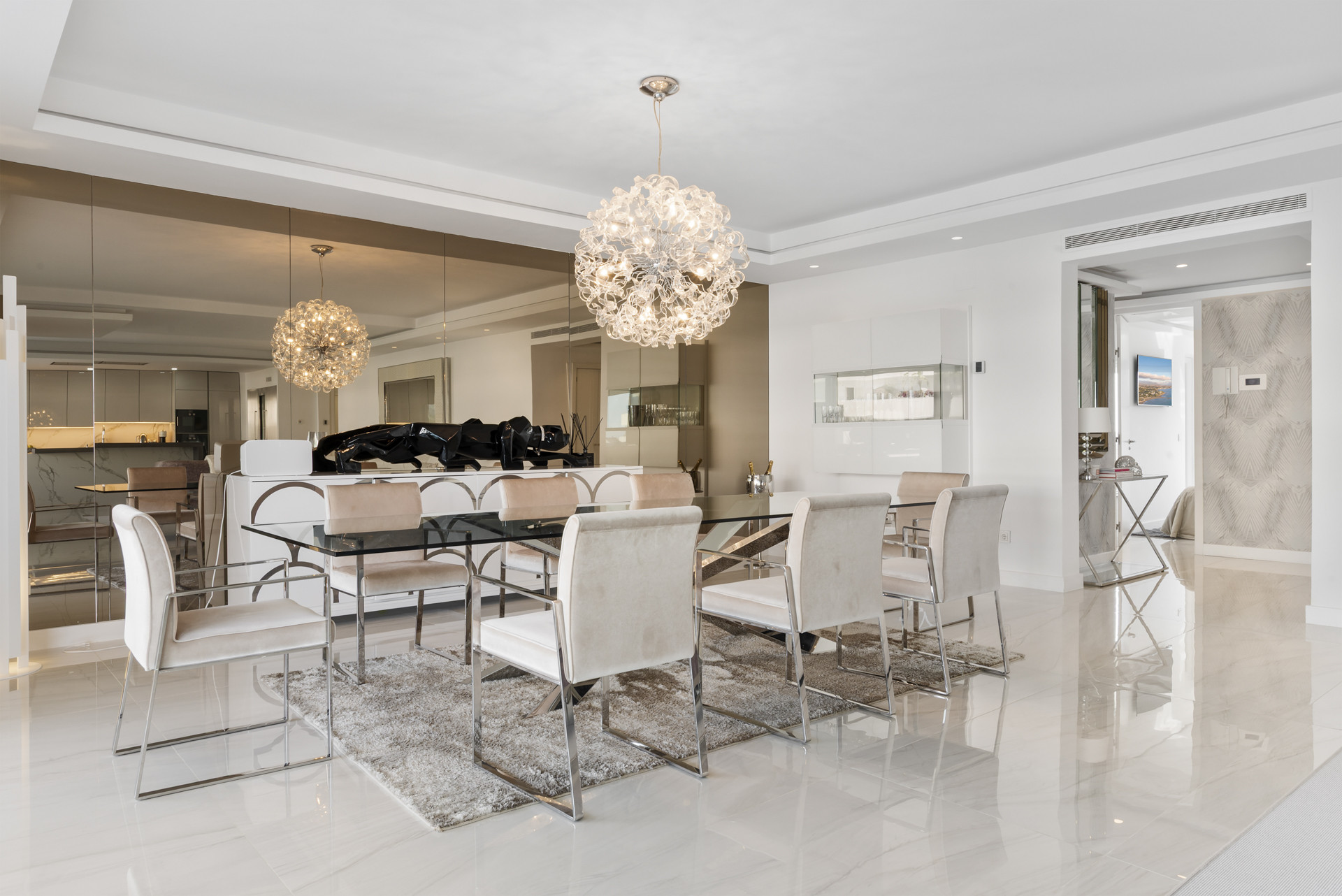 Dining area with modern chairs, glass table, and decorative lighting fixtures.