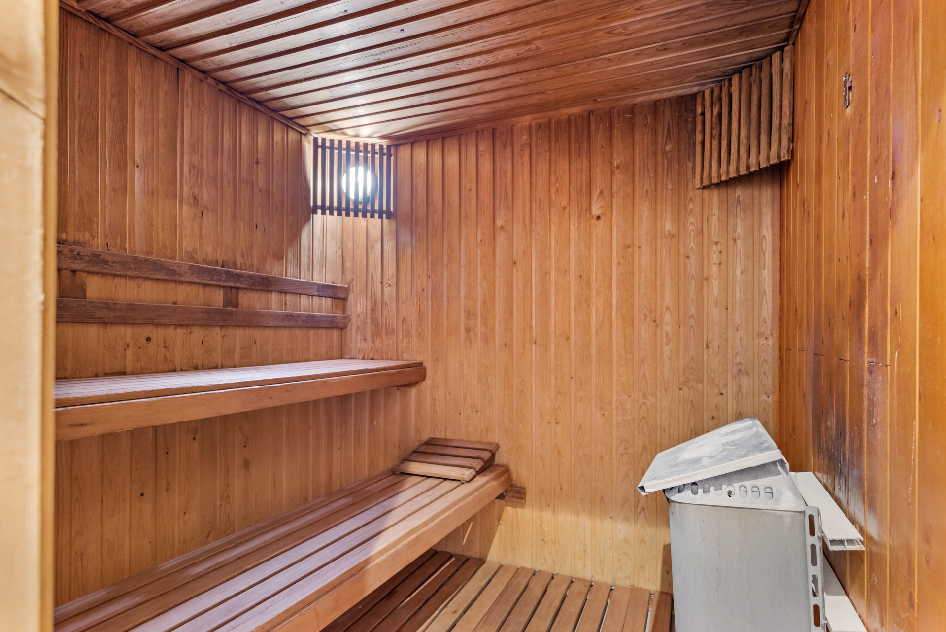Wood-paneled sauna featuring wooden benches and a metal heater in the corner.