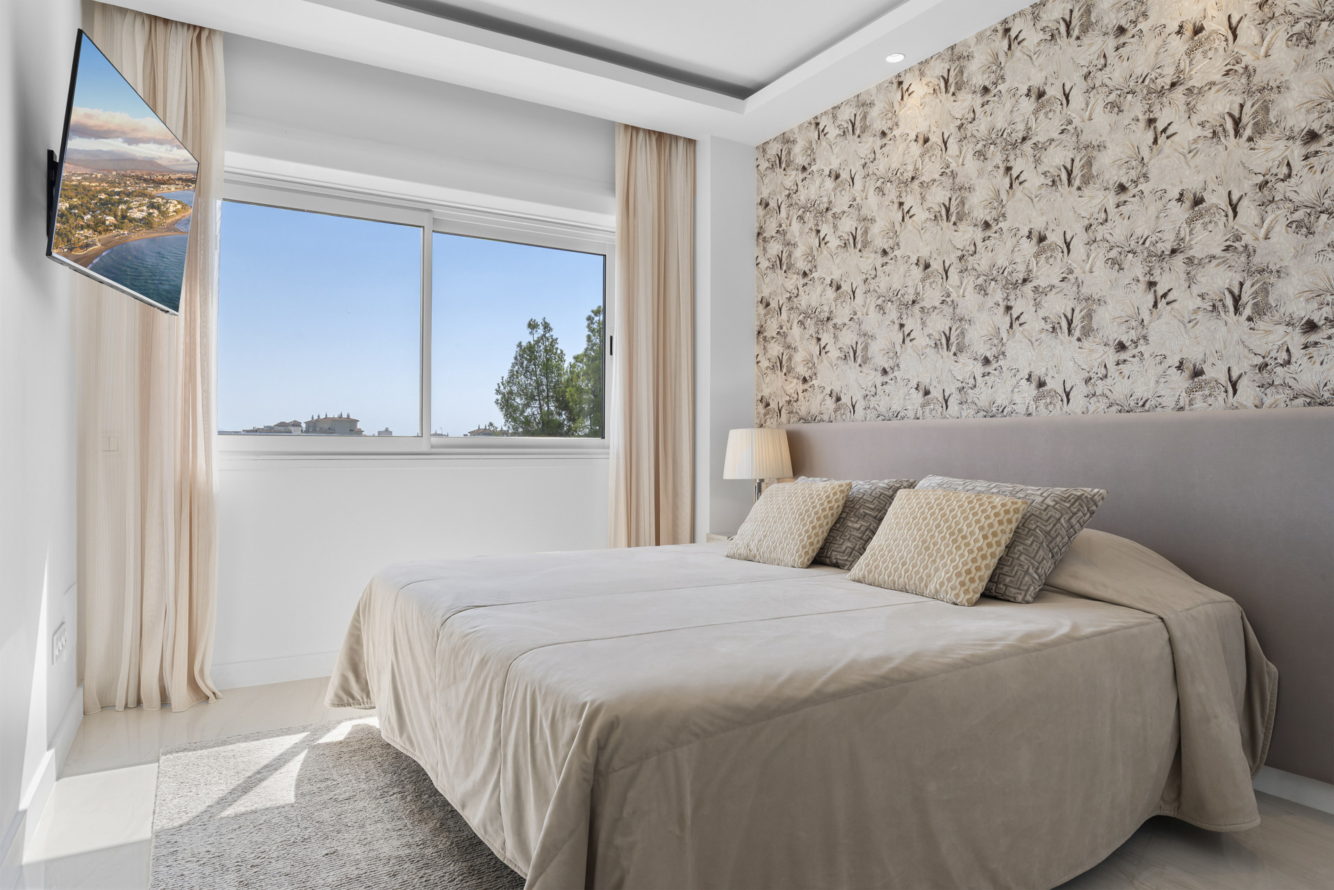 Bright bedroom with patterned wallpaper and window showing trees outside.
