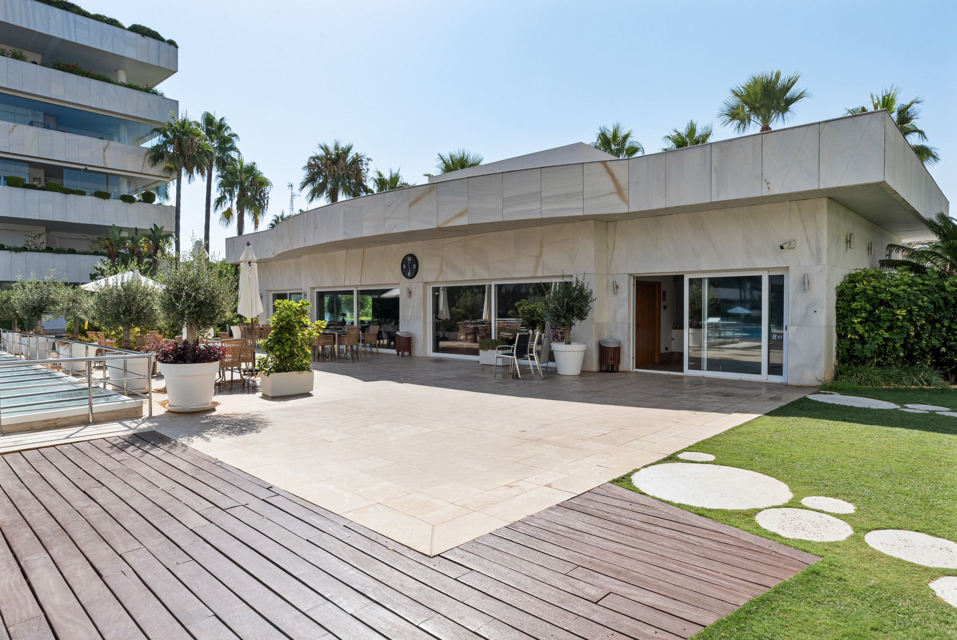 Terrace area with dining furniture and tropical plants leading to a building entrance.
