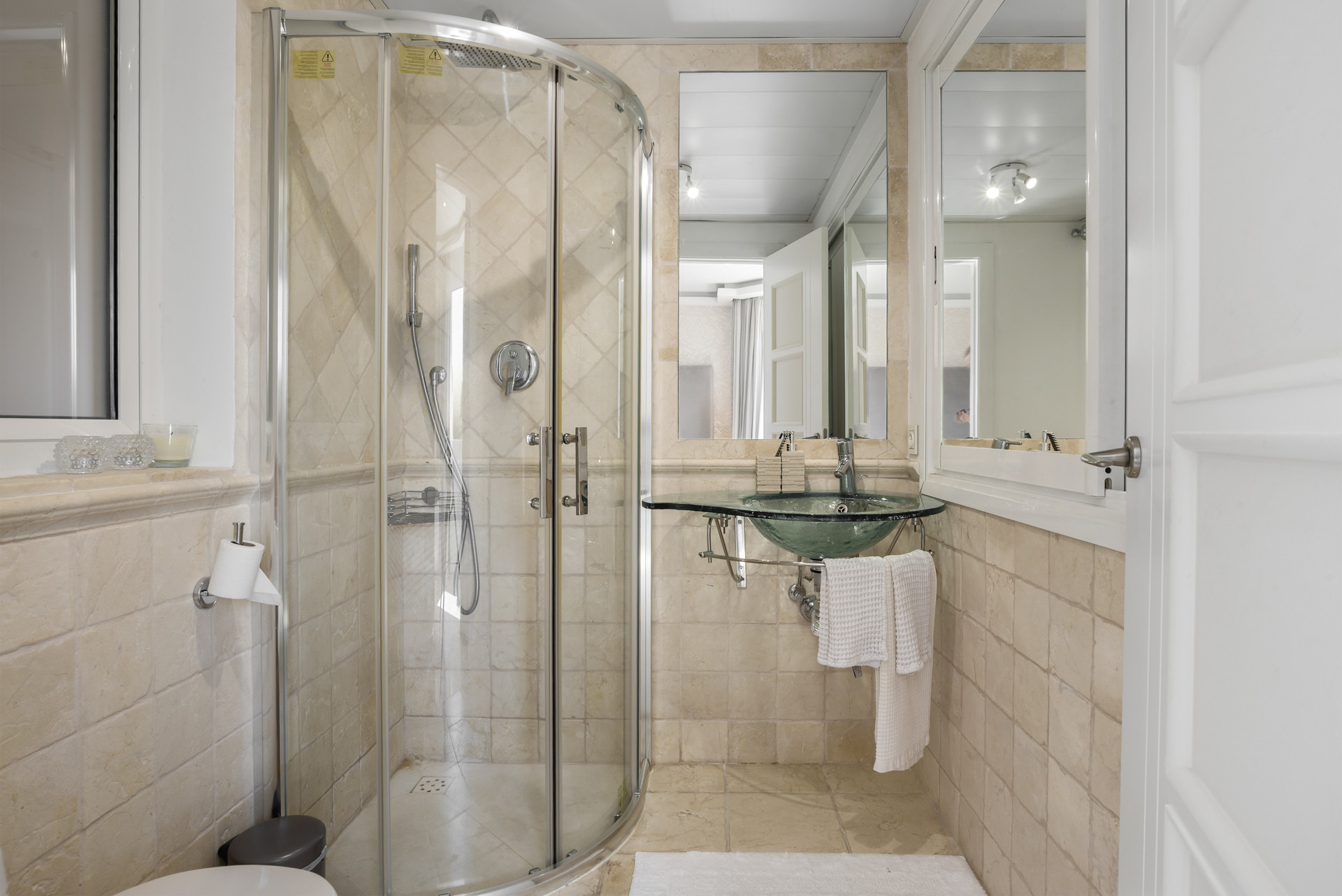A bathroom with a curved shower, glass sink, and beige stone tiles.