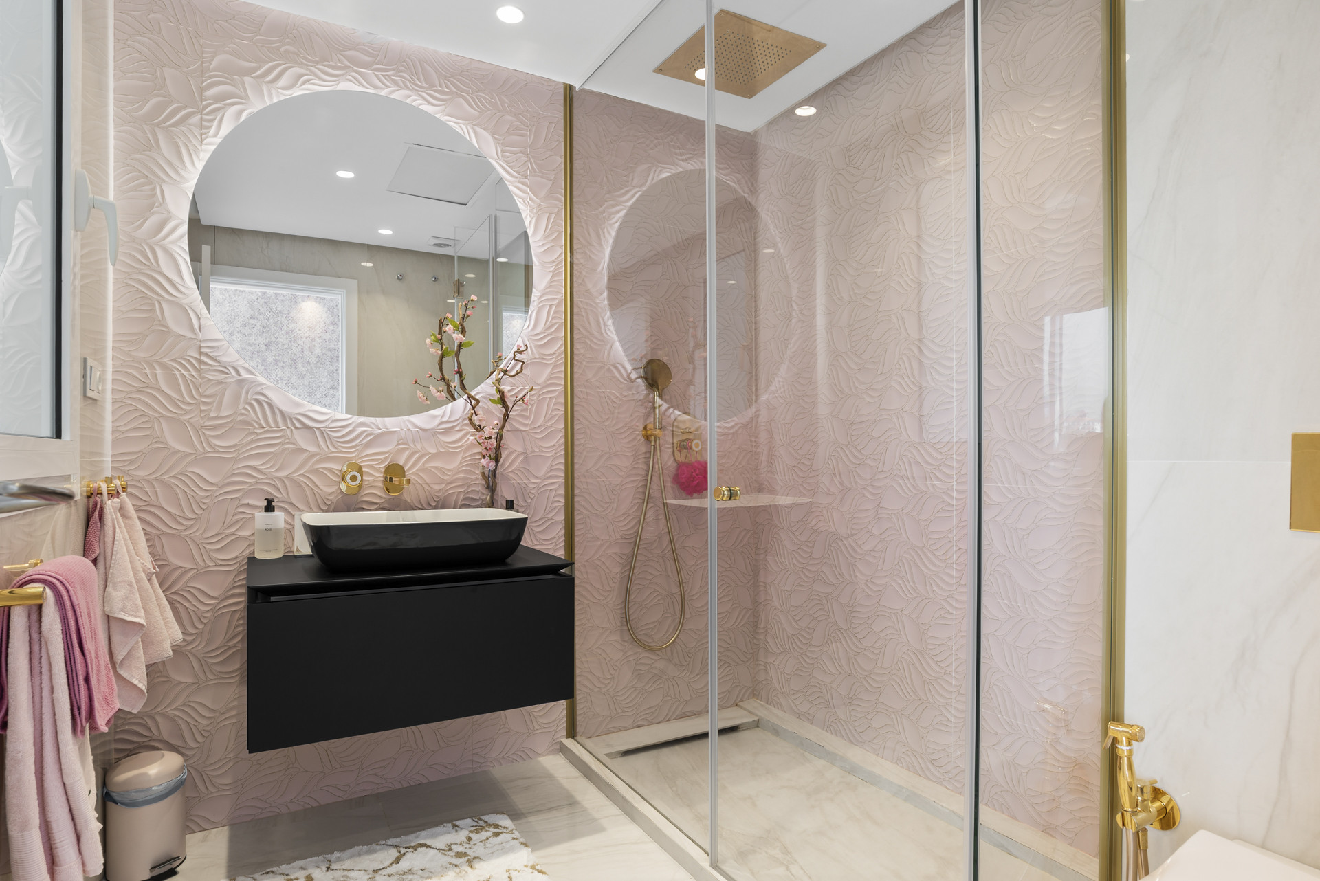 A modern bathroom featuring a glass shower, circular mirror, and textured pink wall.