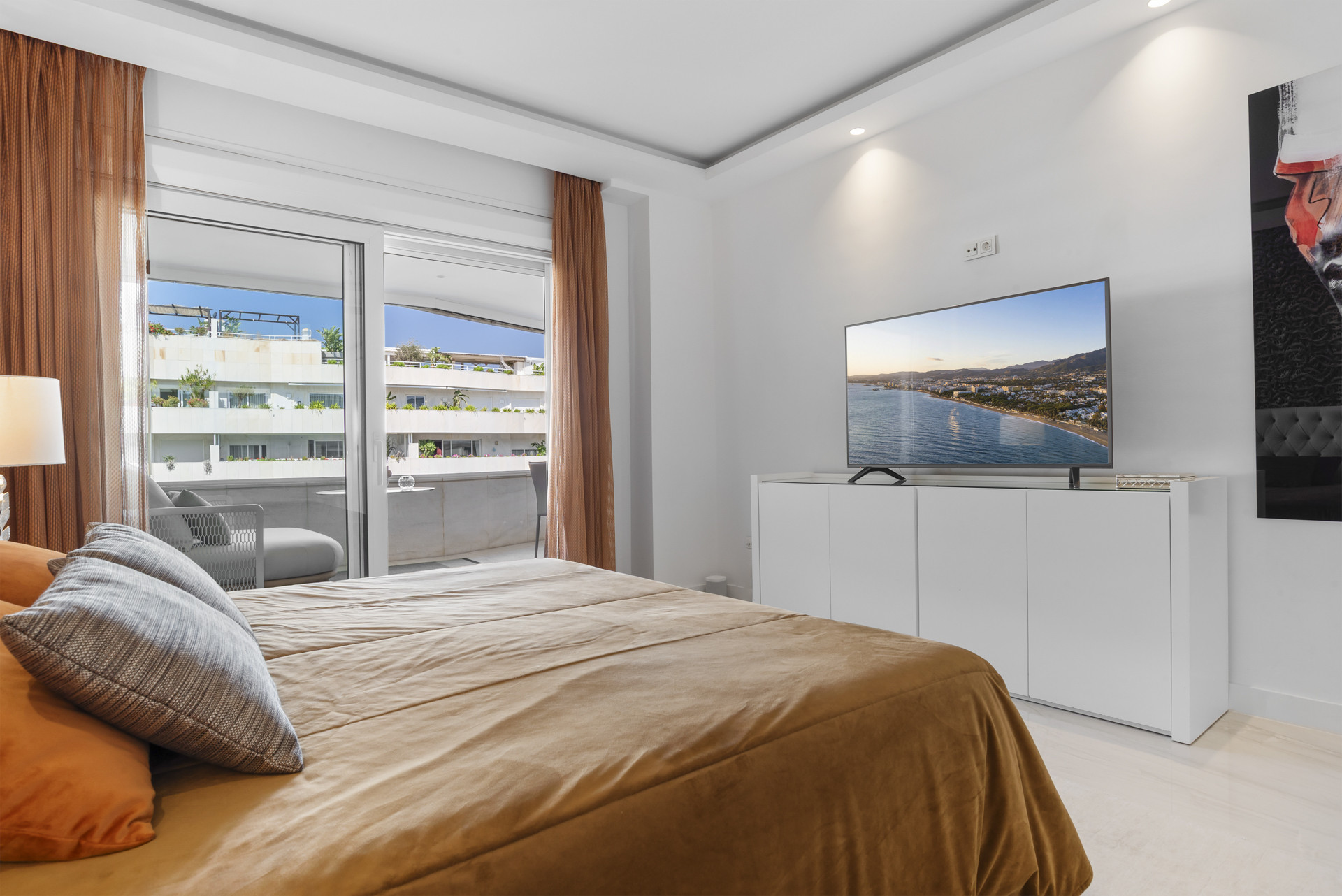 Cozy bedroom with TV, white cabinet, and balcony view of neighboring buildings.