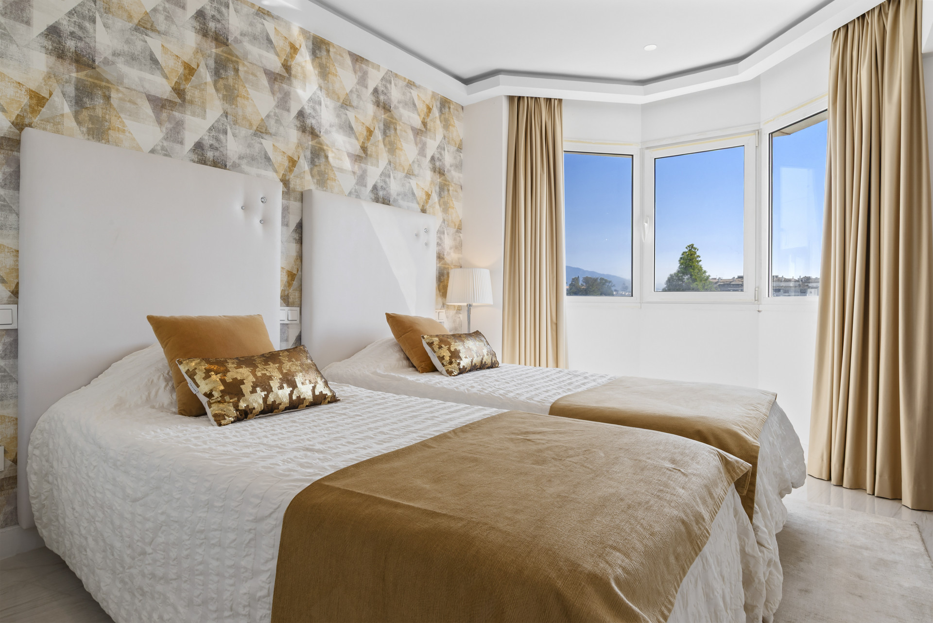 Well-lit bedroom with two twin beds, decorative pillows, and large windows offering views.