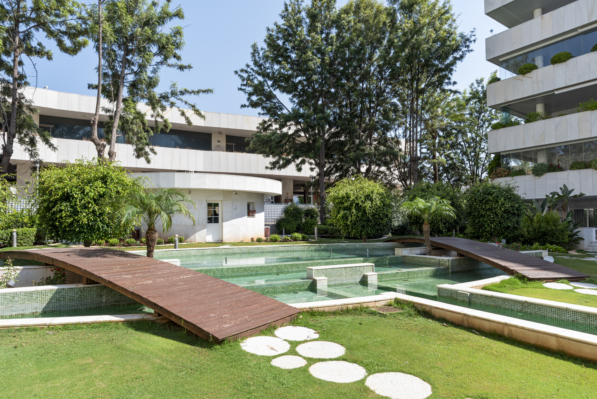 Outdoor area with wooden bridge over a water feature and landscaped greenery.