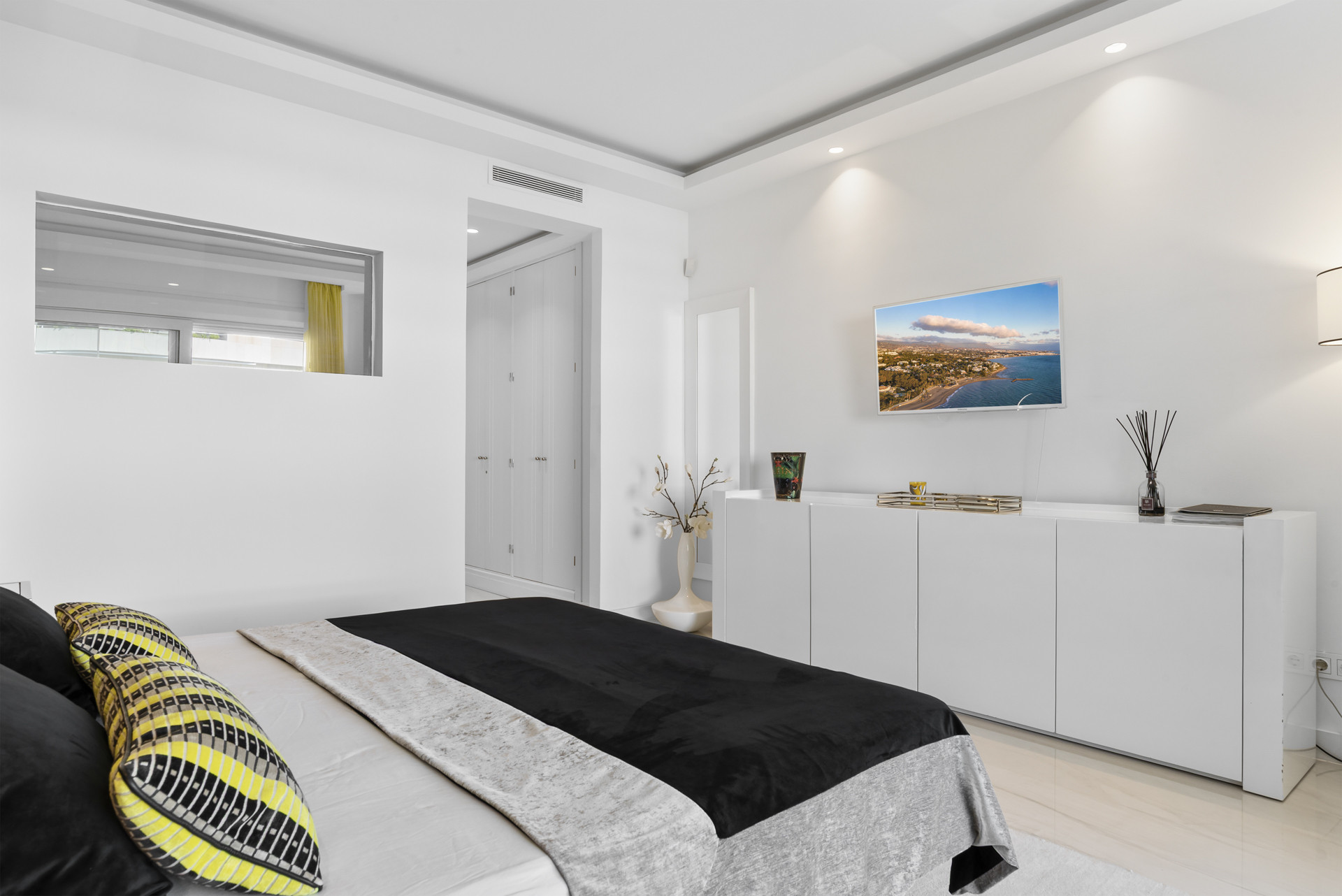 Bright bedroom features modern decor and a wall-mounted TV adjacent to spacious wardrobes.