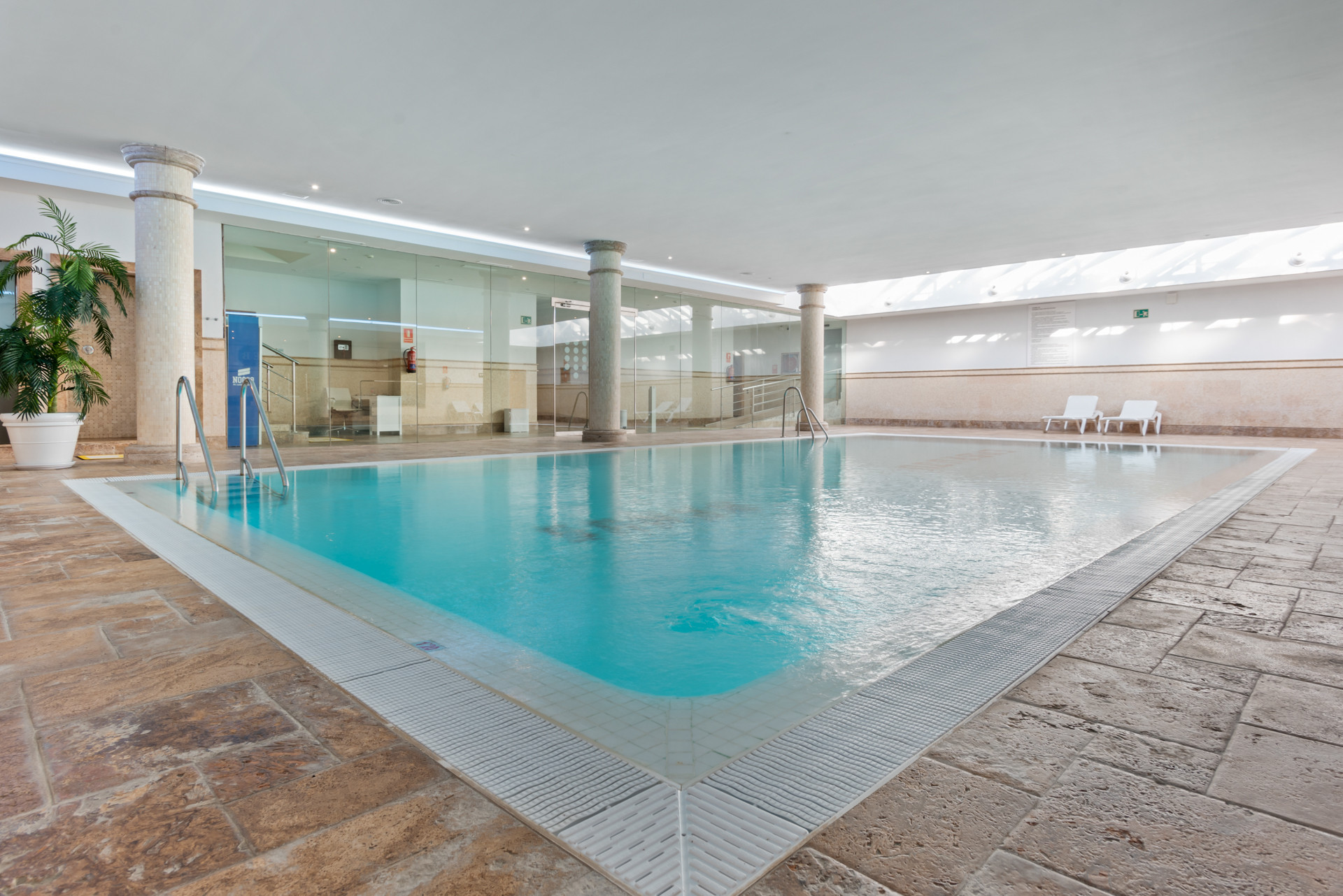 Indoor swimming pool with glass walls and tiled flooring.