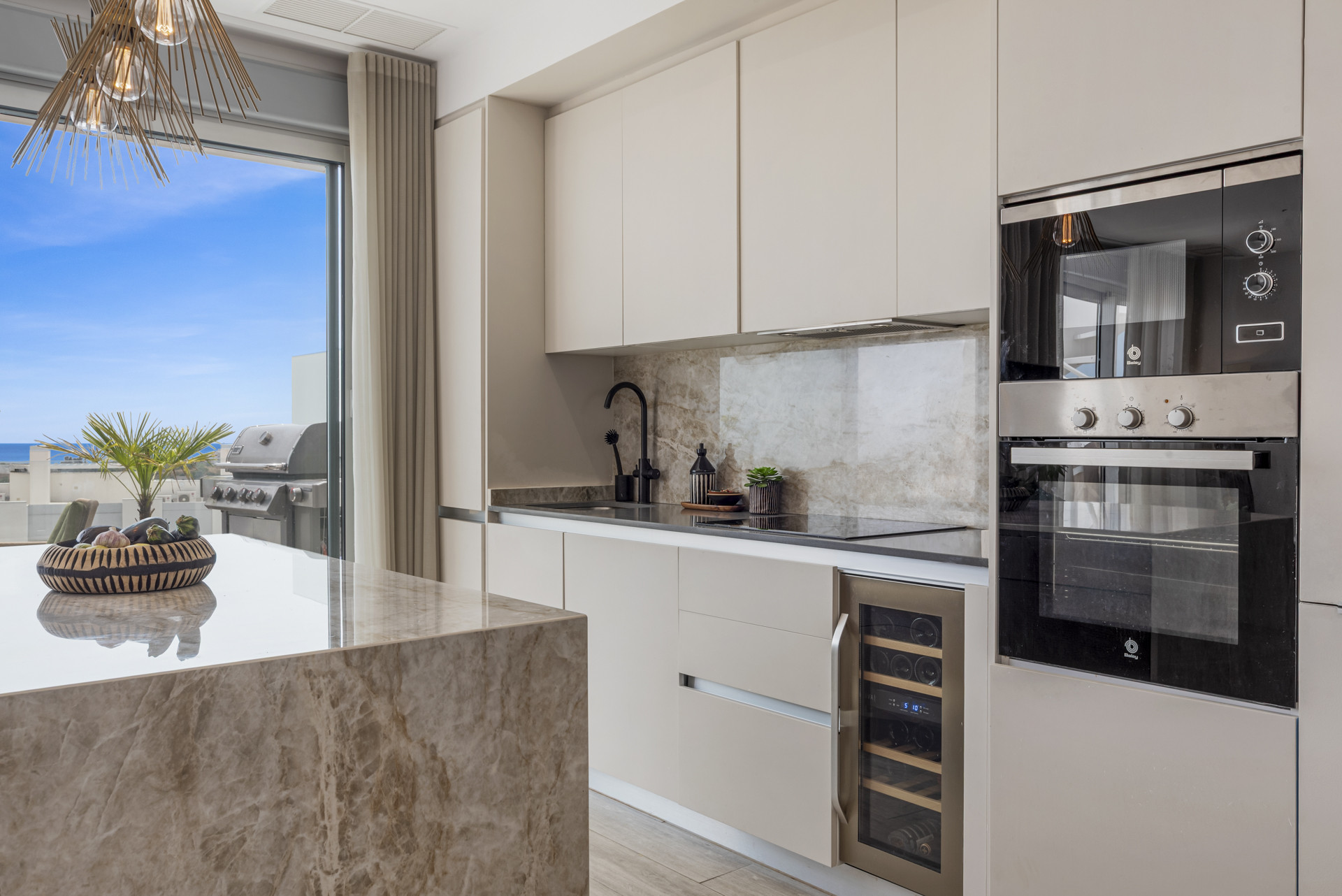 Modern kitchen with beige cabinetry, built-in appliances, a marble island, and a wine cooler.
