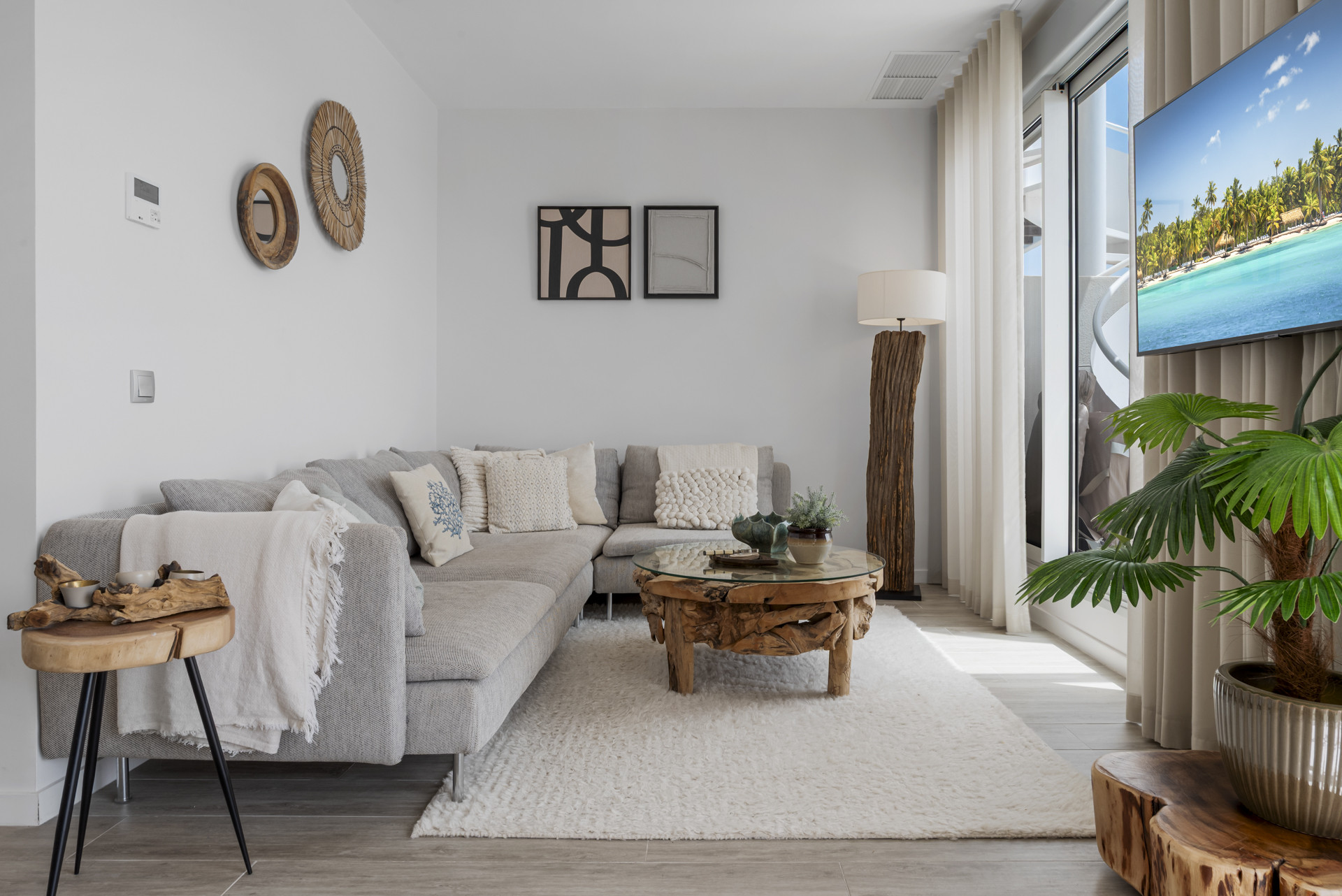 Living room with a grey sectional sofa, glass and wood coffee table, and a wall-mounted TV.