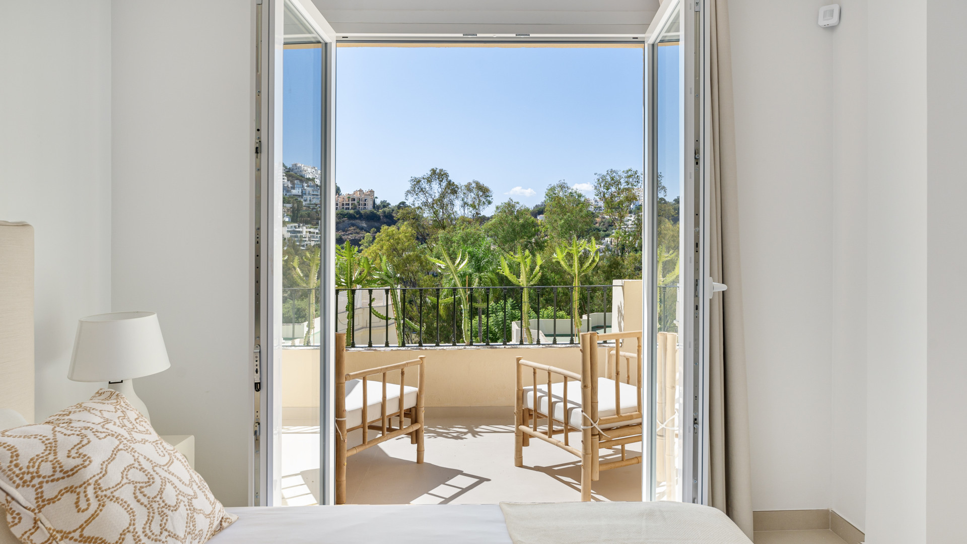 View from inside a bedroom showcasing a balcony with two outdoor chairs and greenery.