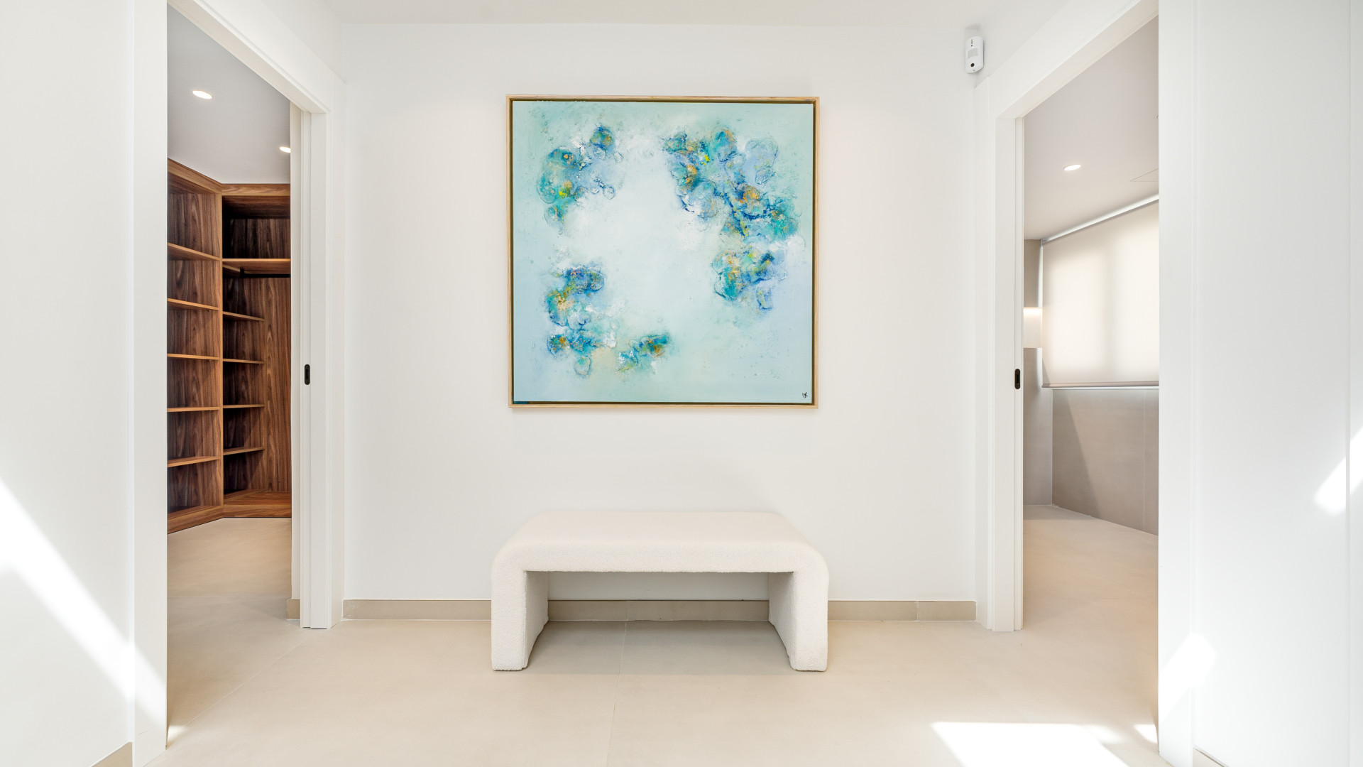 Stylish hallway with a white bench and a framed blue artwork. Doors lead to a closet and bathroom.