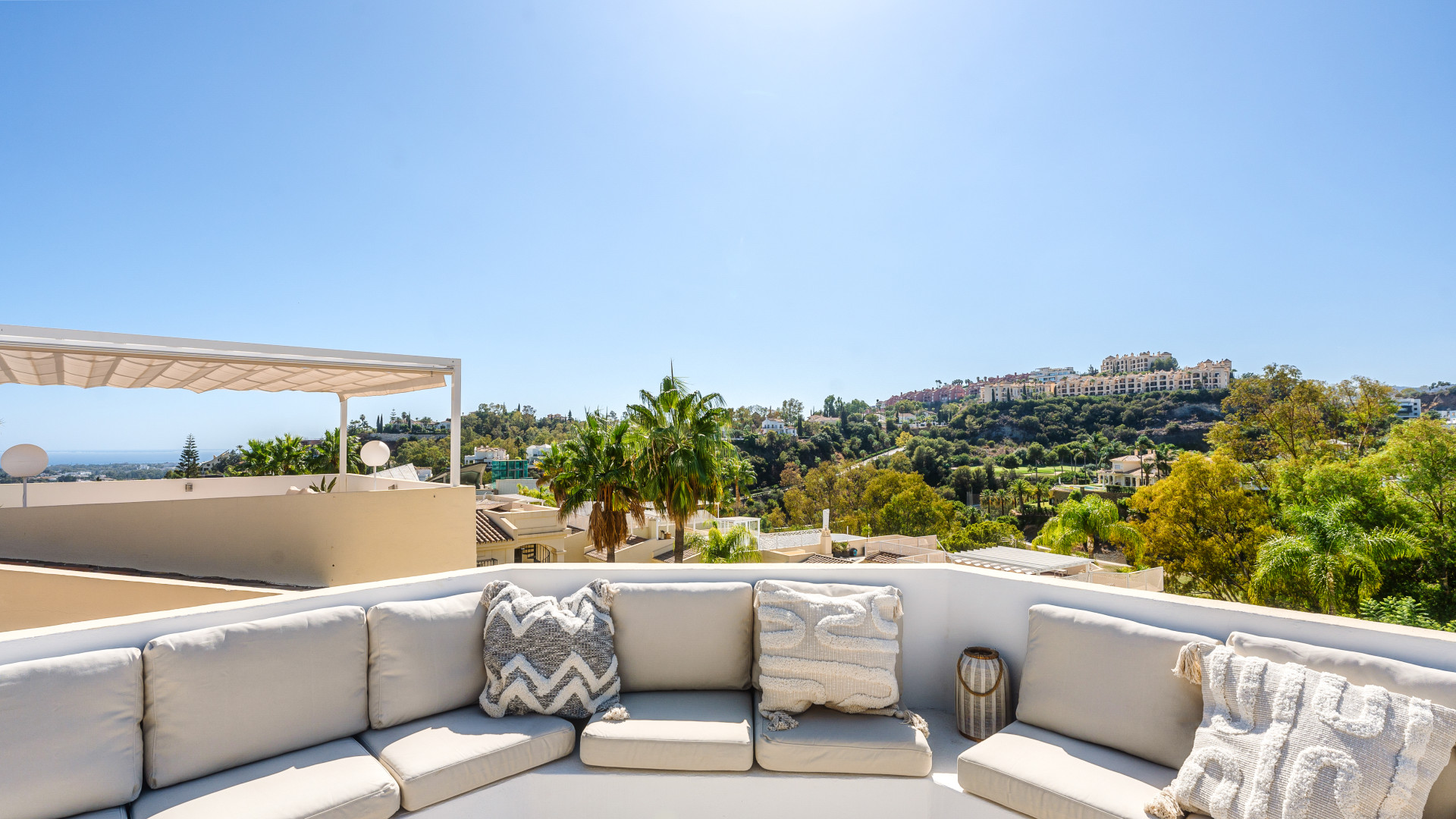 Outdoor lounge area with soft seating, palm trees, and clear blue sky above.