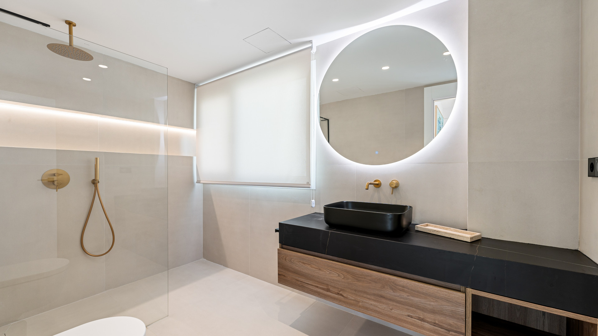Modern bathroom with shower, round mirror, and wooden vanity in neutral tones.